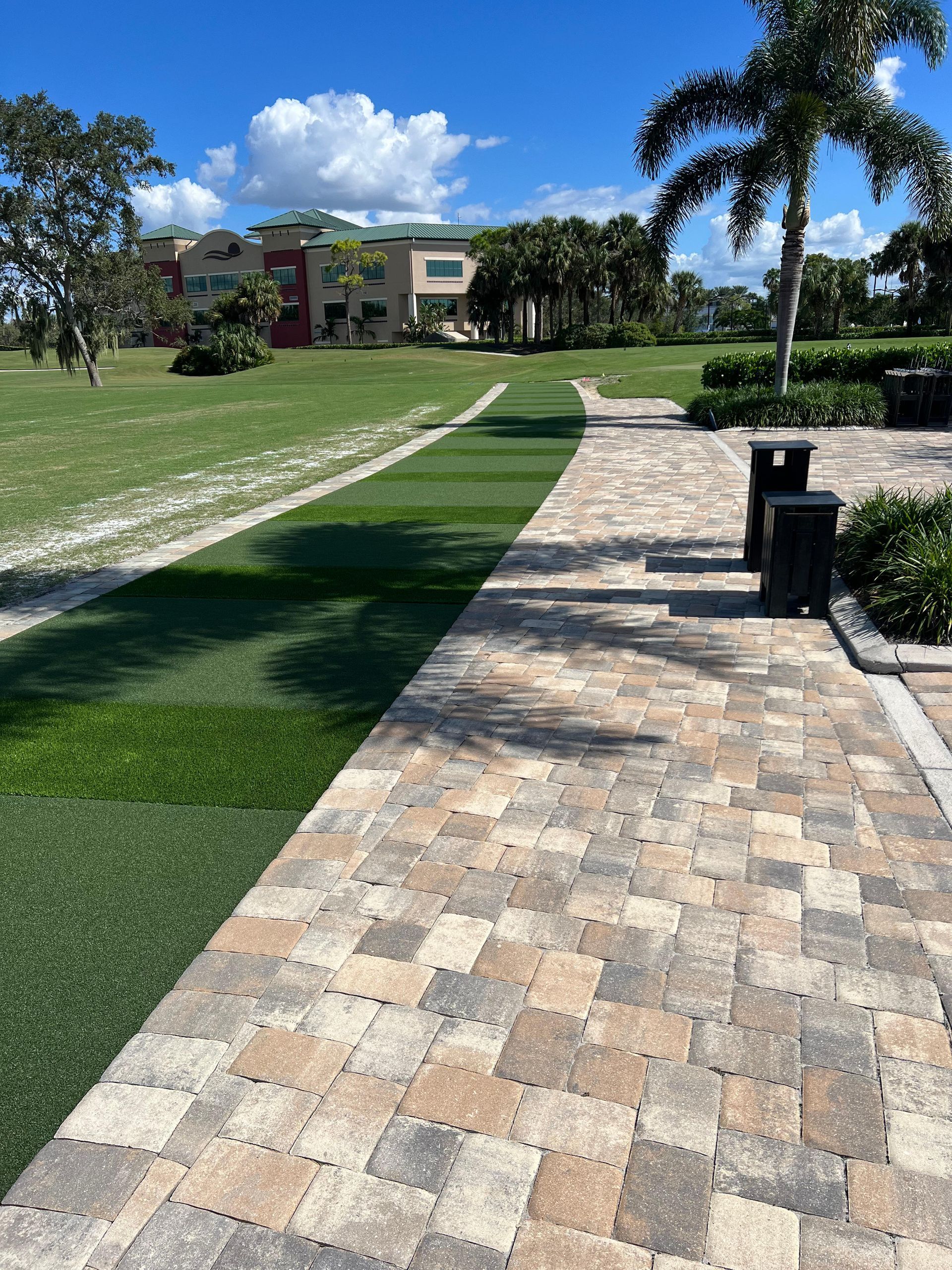 A brick walkway leading to a grassy field with a building in the background.