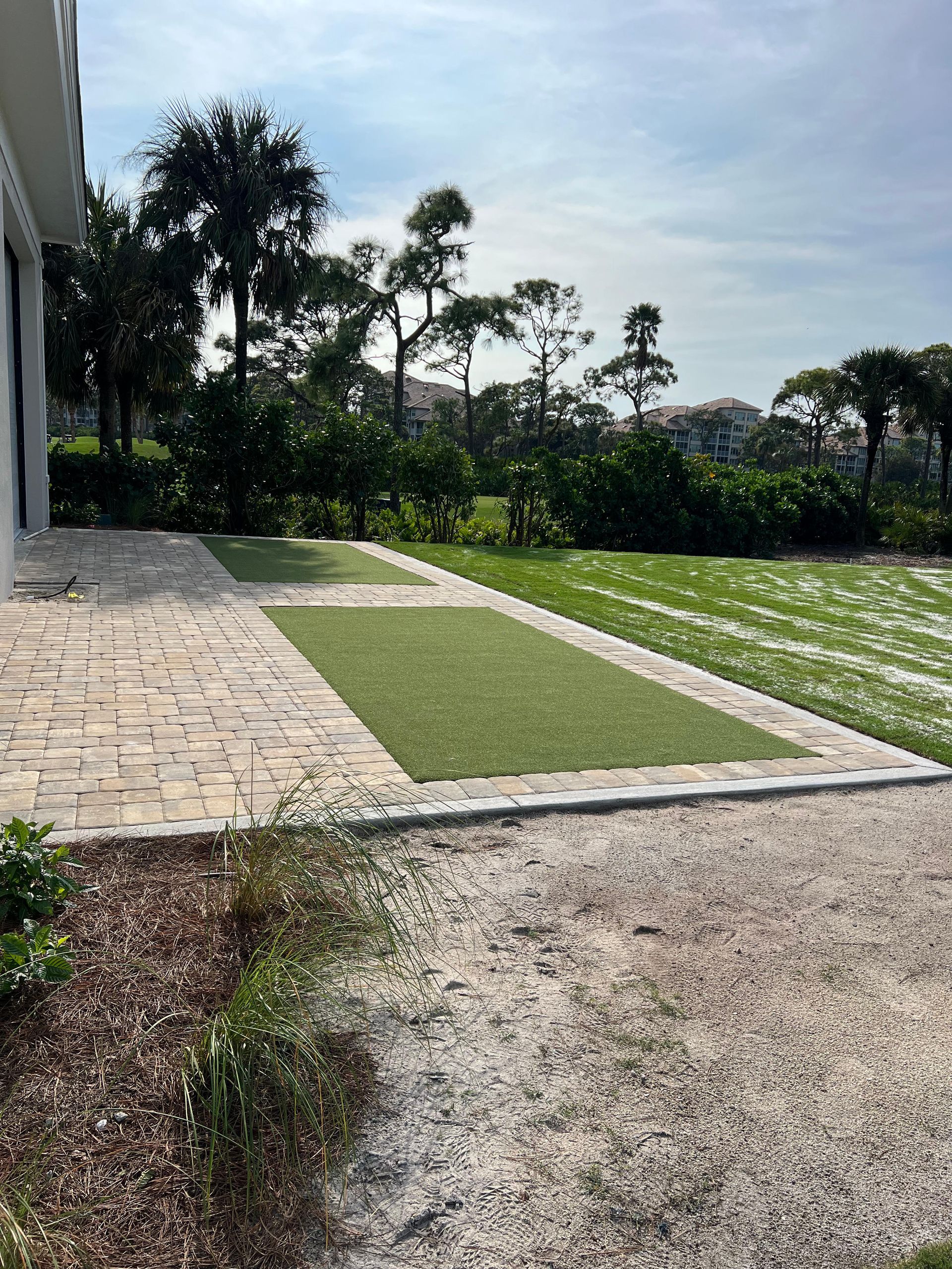 A brick walkway leading to a lush green field with trees in the background.