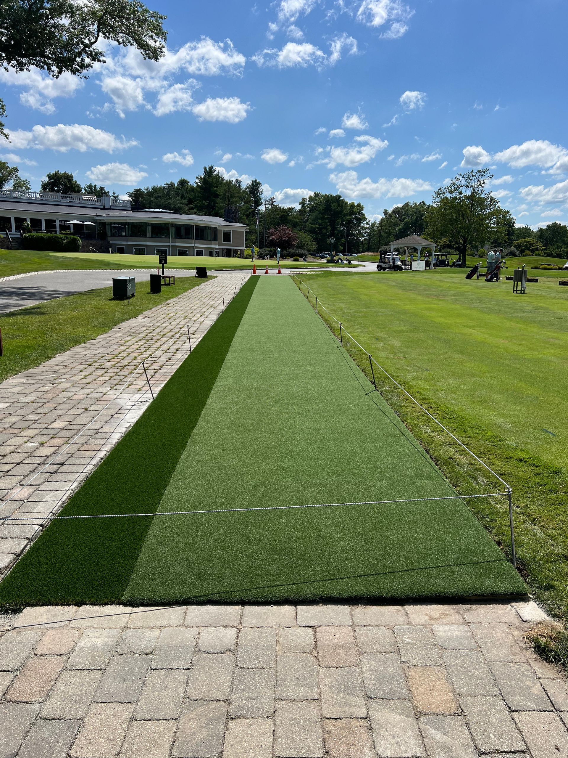 A brick walkway leading to a grassy field with a house in the background.