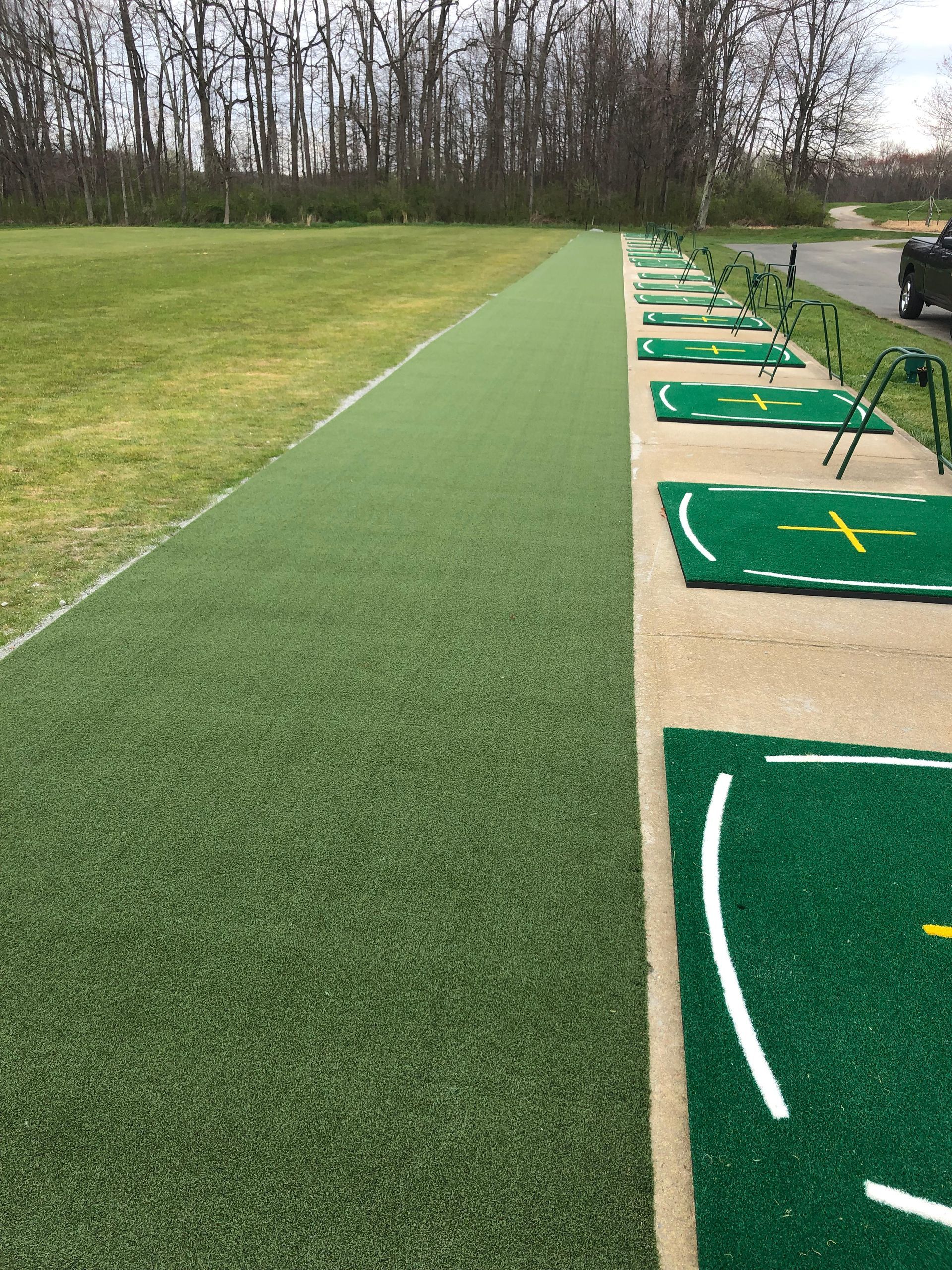 A row of green mats on a golf course with trees in the background.