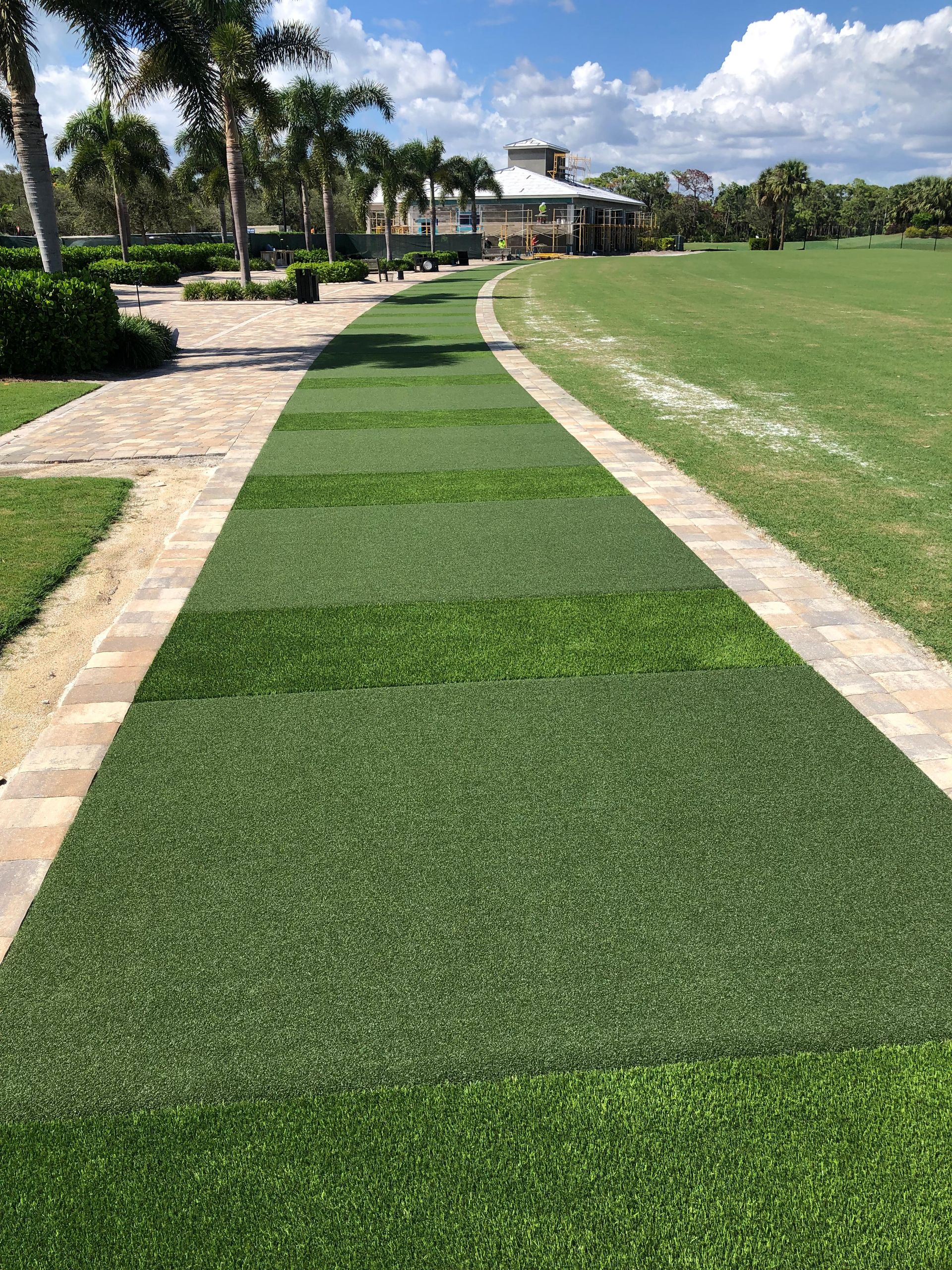 A brick walkway leading to a grassy field with a house in the background.