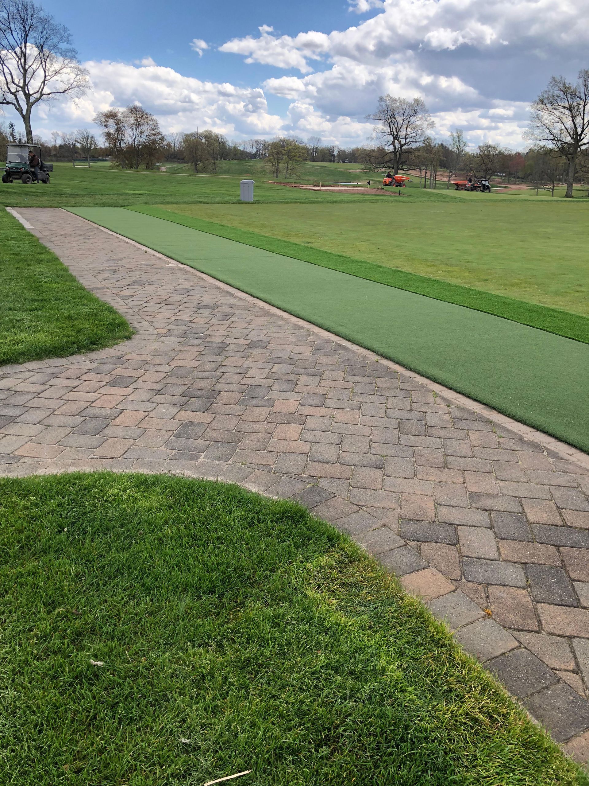 A brick walkway leading to a golf course on a sunny day.