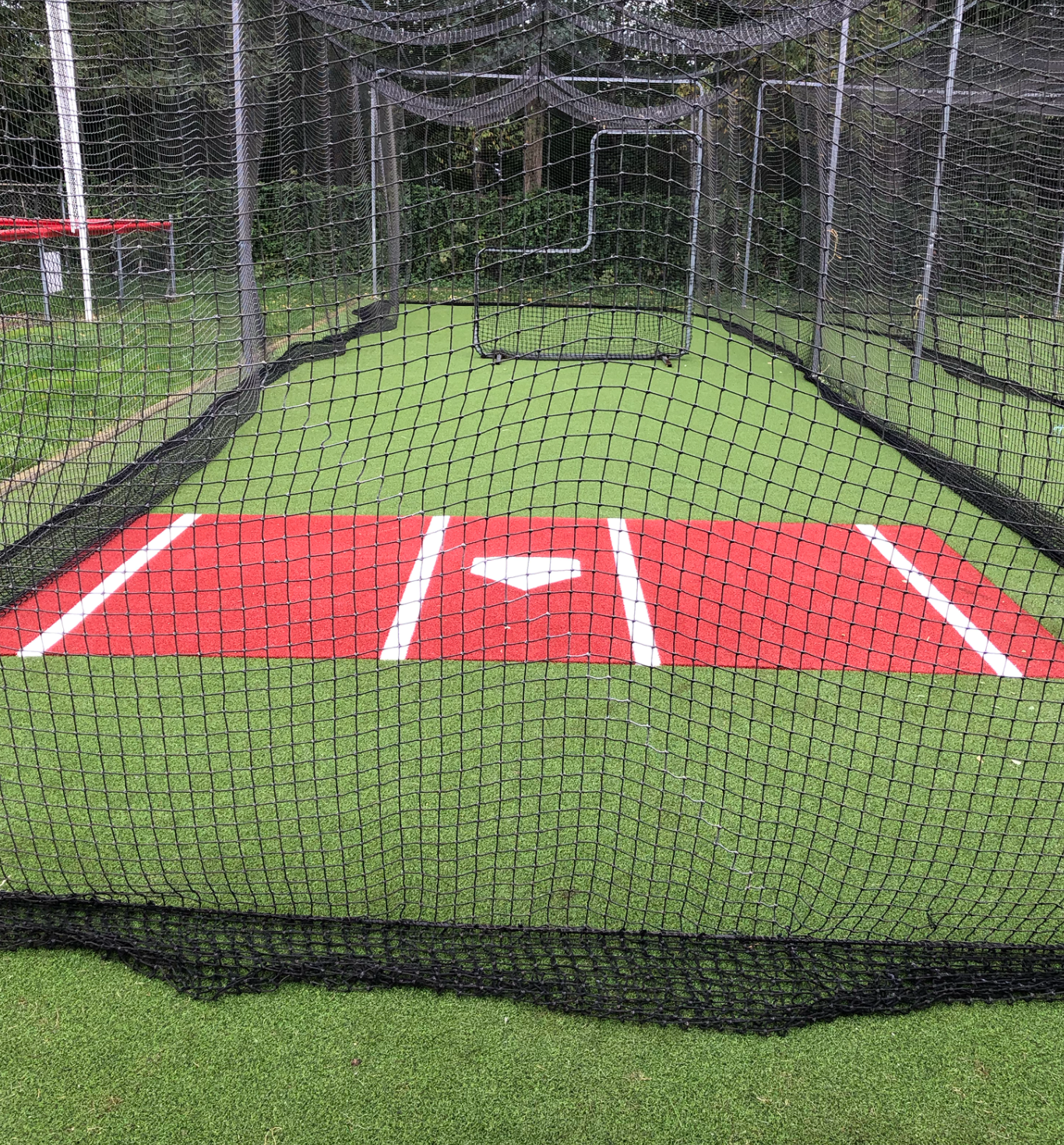 A baseball field with a batting cage and a red base.