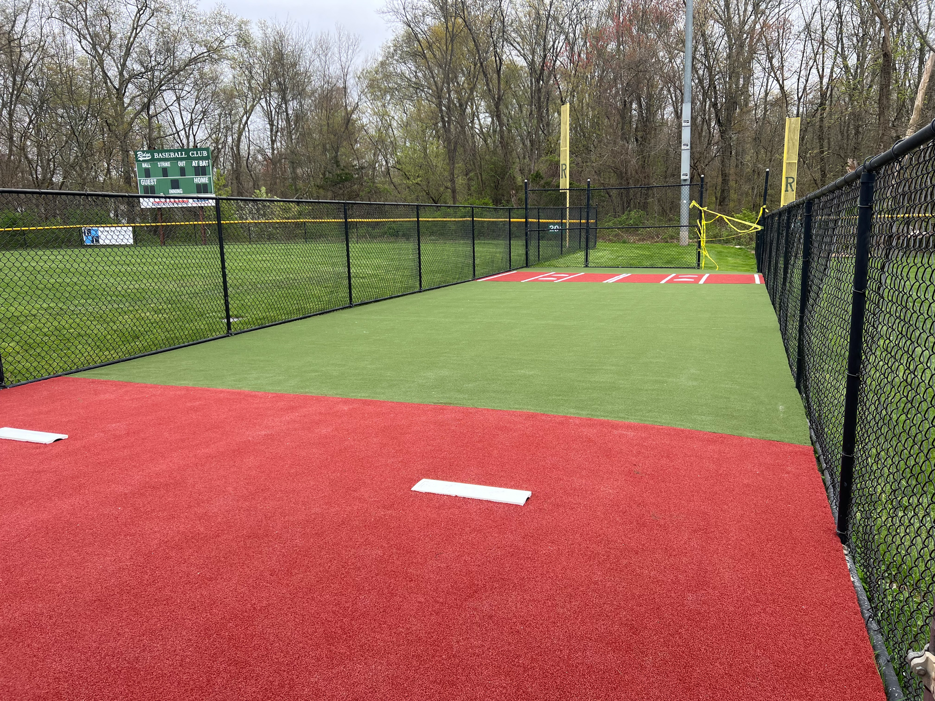 A baseball field with a fence around it and trees in the background.