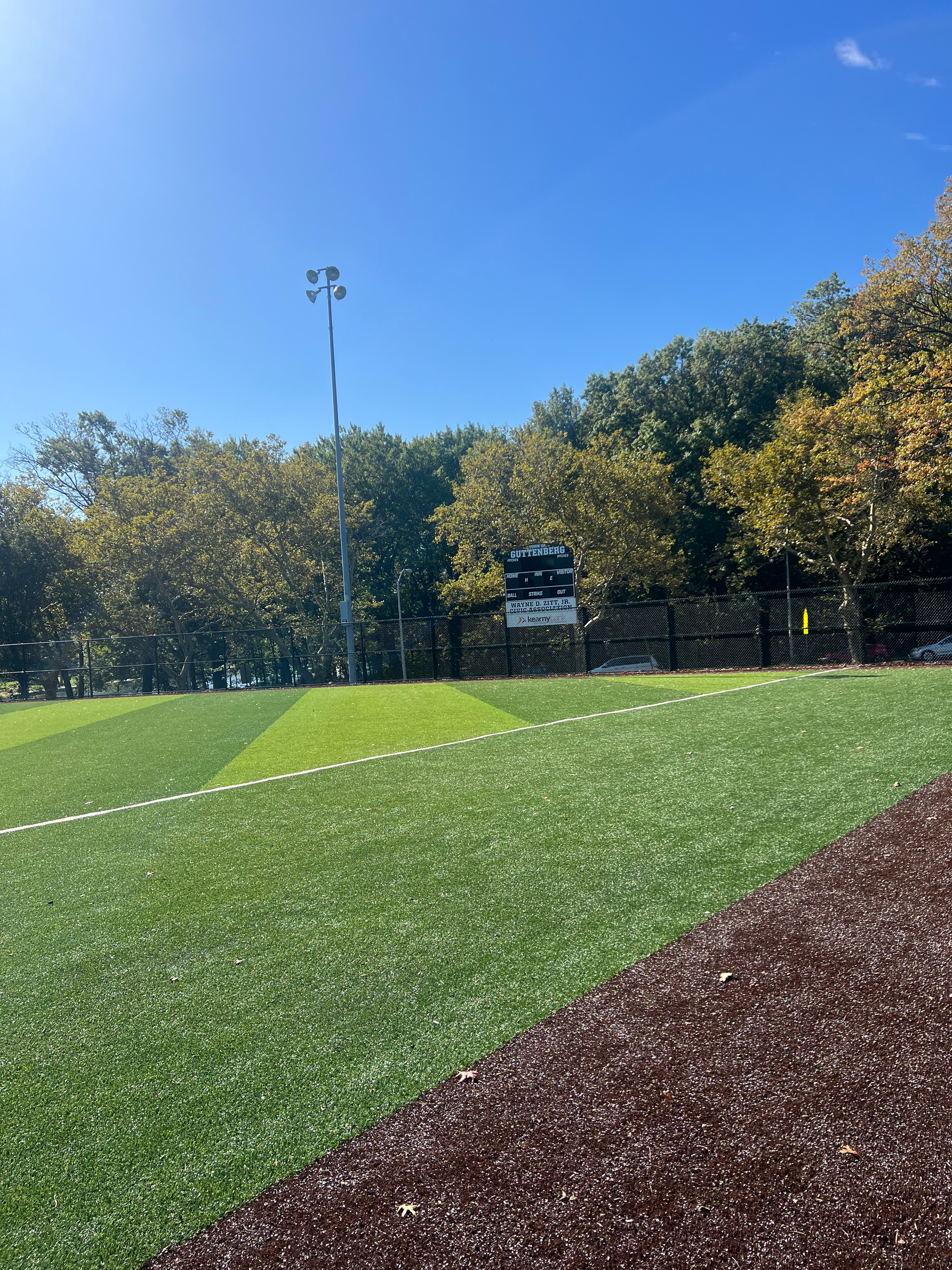 A baseball field with a scoreboard in the background and trees in the background.