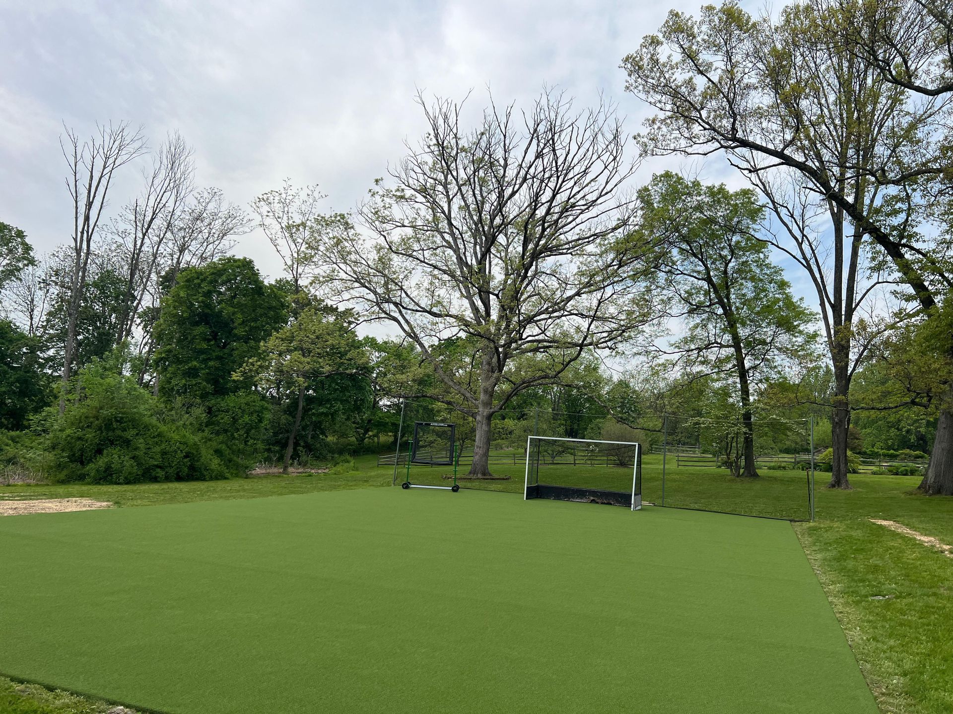 A soccer field with a goal in the middle of a park surrounded by trees.