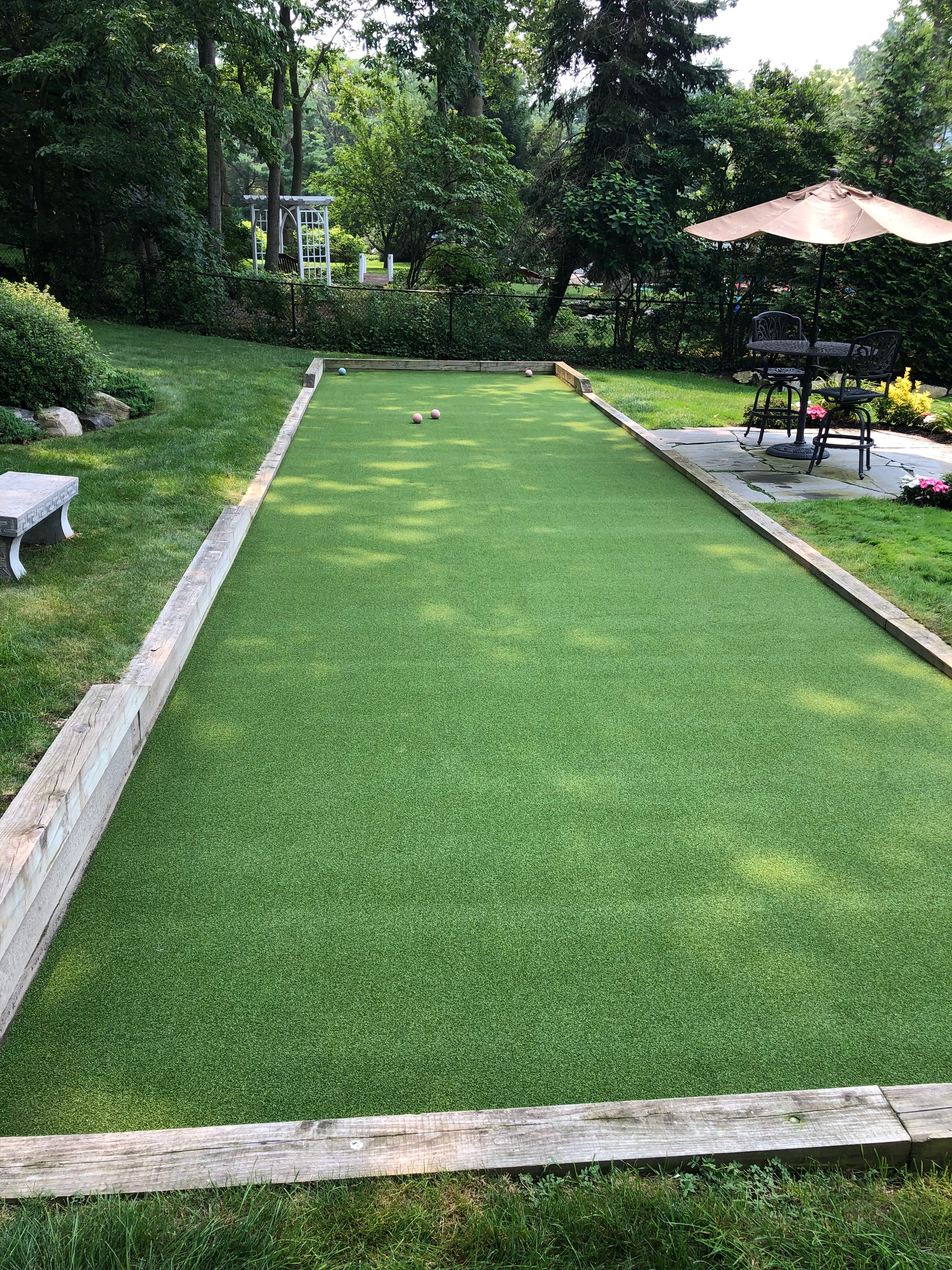 A bocce ball court in a backyard with a picnic table and umbrellas.