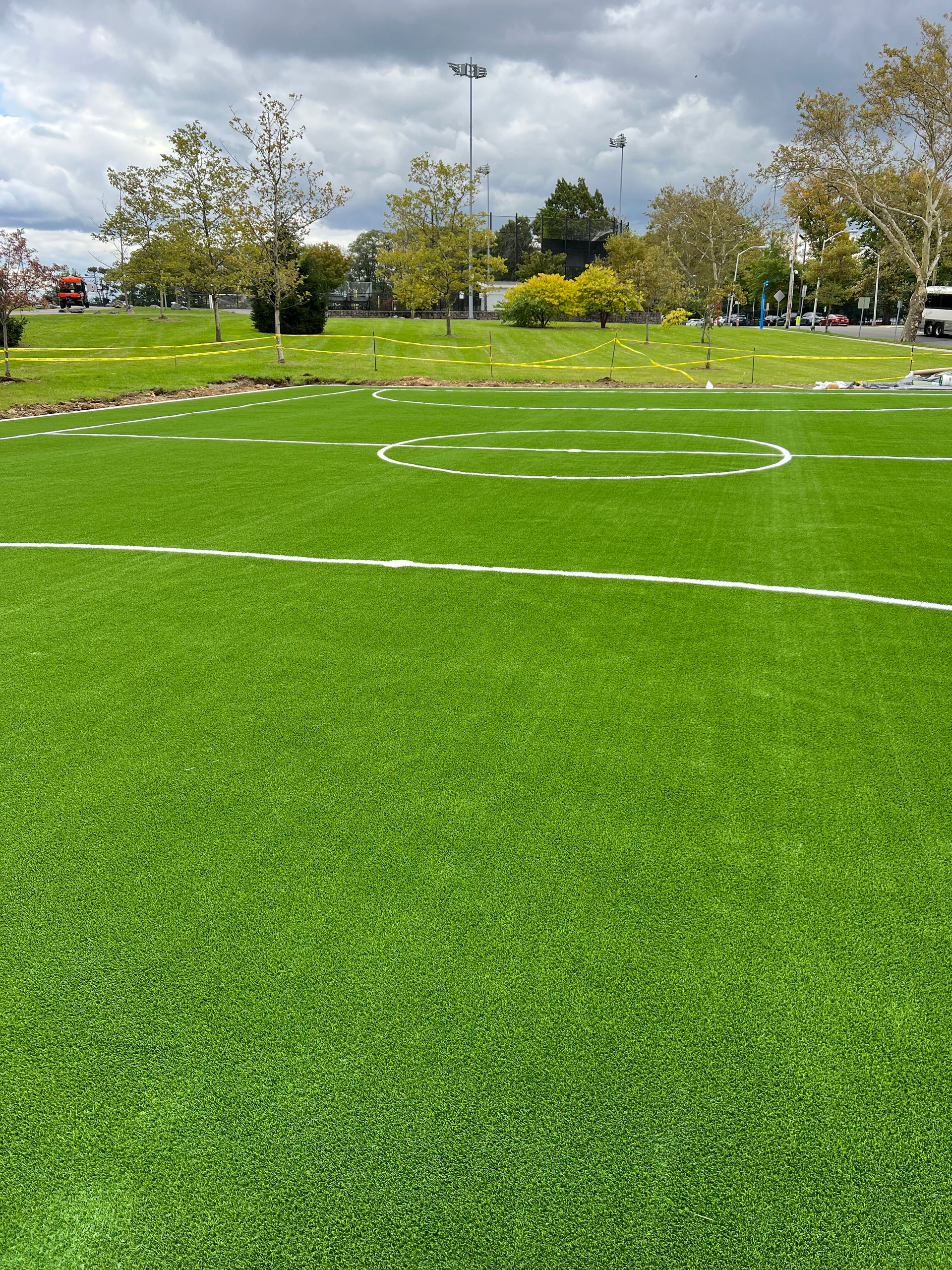 A soccer field with a few trees in the background and a cloudy sky.