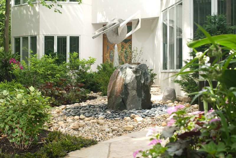 Water fountain surrounded by greenery, front of a modern white building.