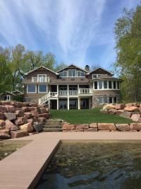 Large stone and brown house on a lake with a dock and terraced stone landscaping.