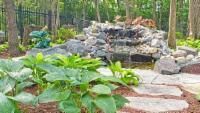 Waterfall feature in a garden with stone path and lush green plants.
