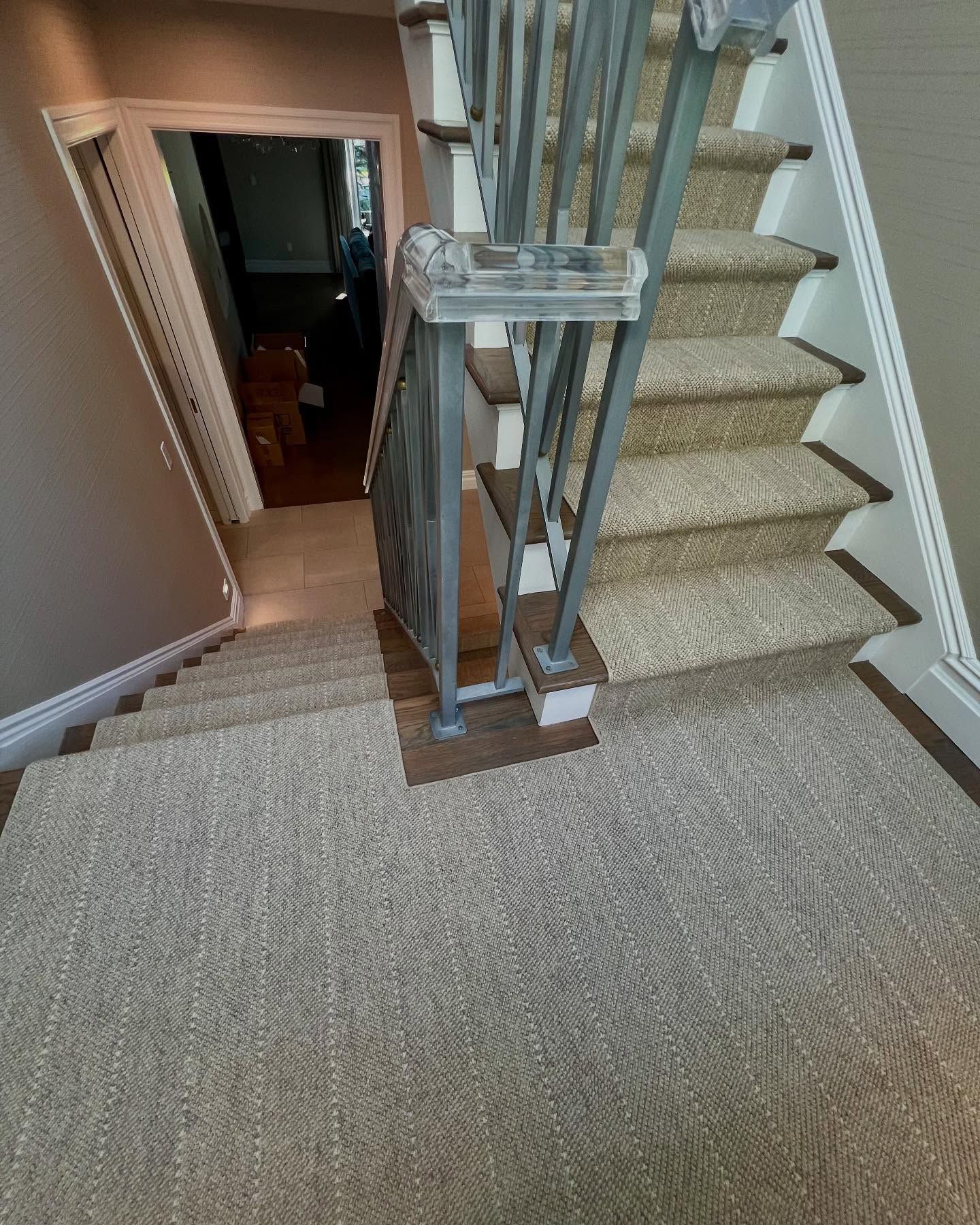 Staircase with carpeted steps and metal railing, leading down to a hallway with a doorway.