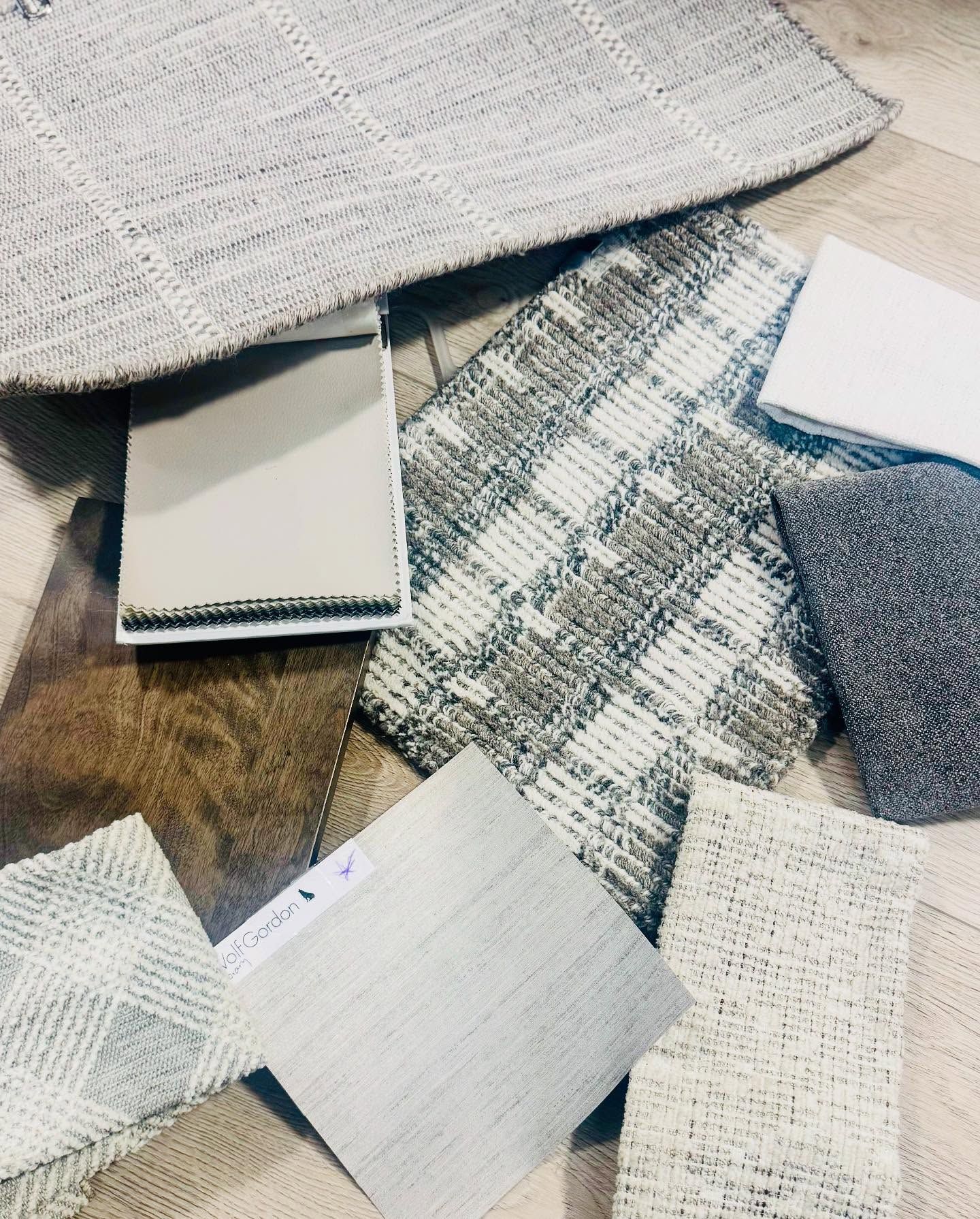 Samples of carpet and material swatches on a wood floor, mostly neutral tones.