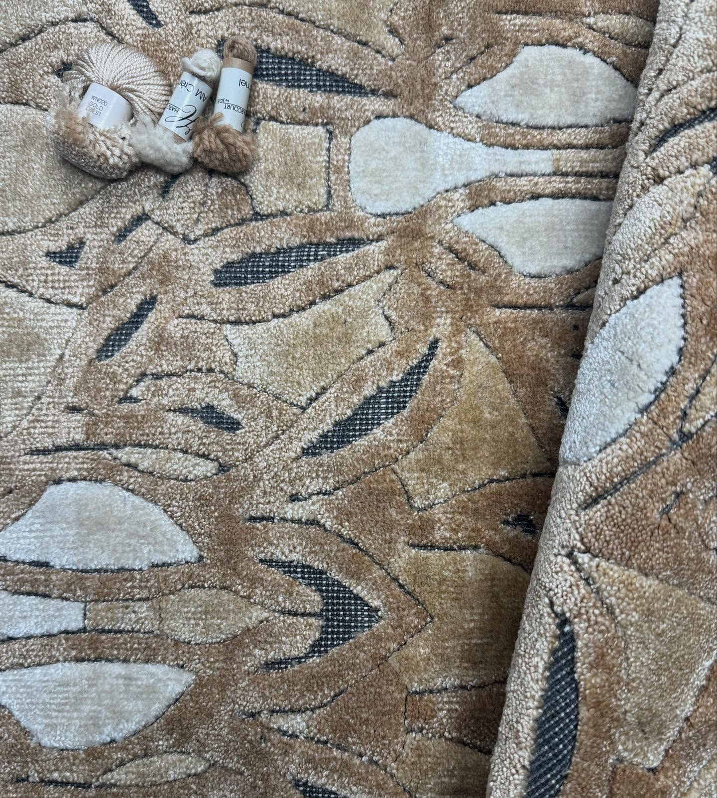 Tan patterned rug with rolled-up corner, showing light and dark shapes. Two small yarn balls on top.