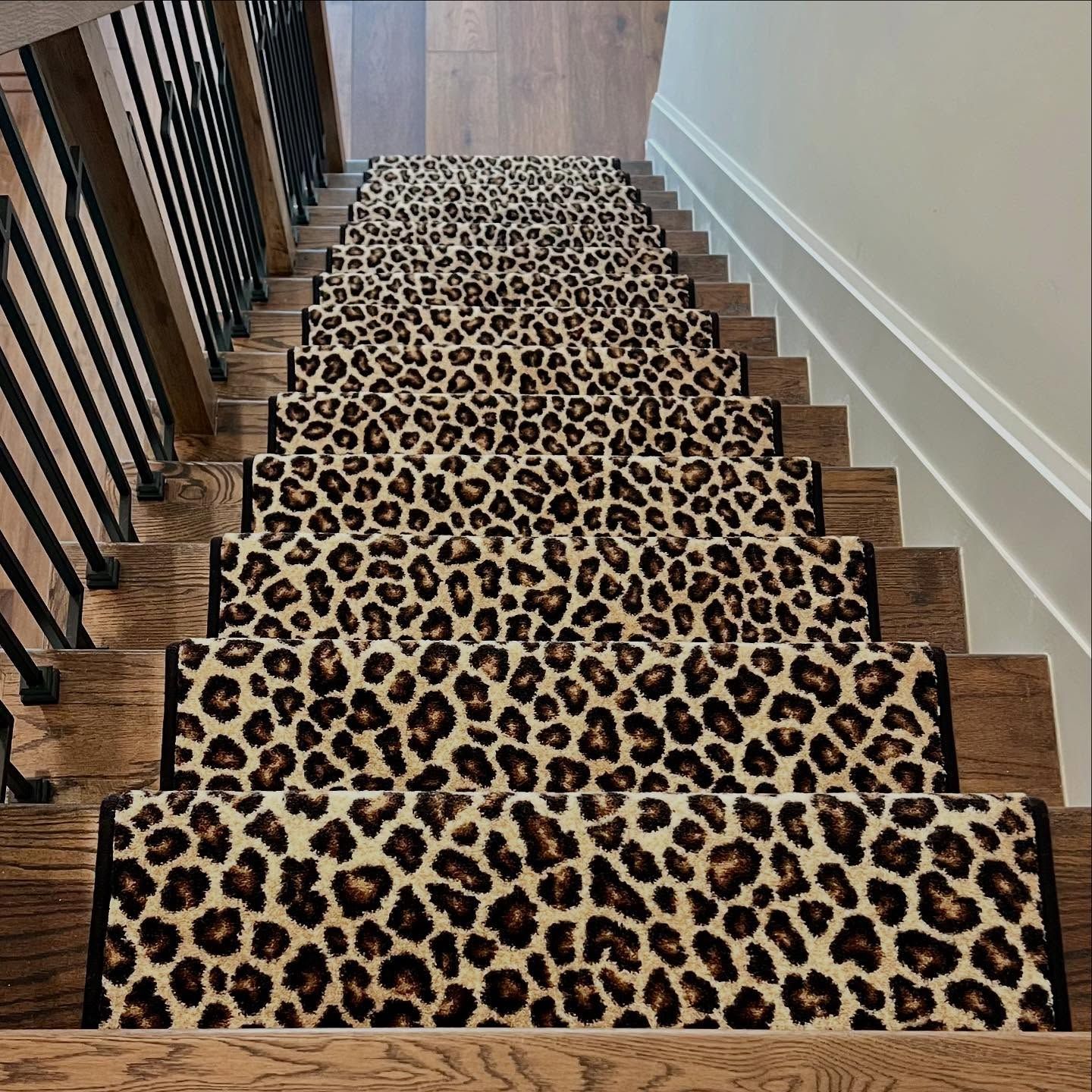 Staircase with leopard print runner. Wooden steps and dark metal railing.