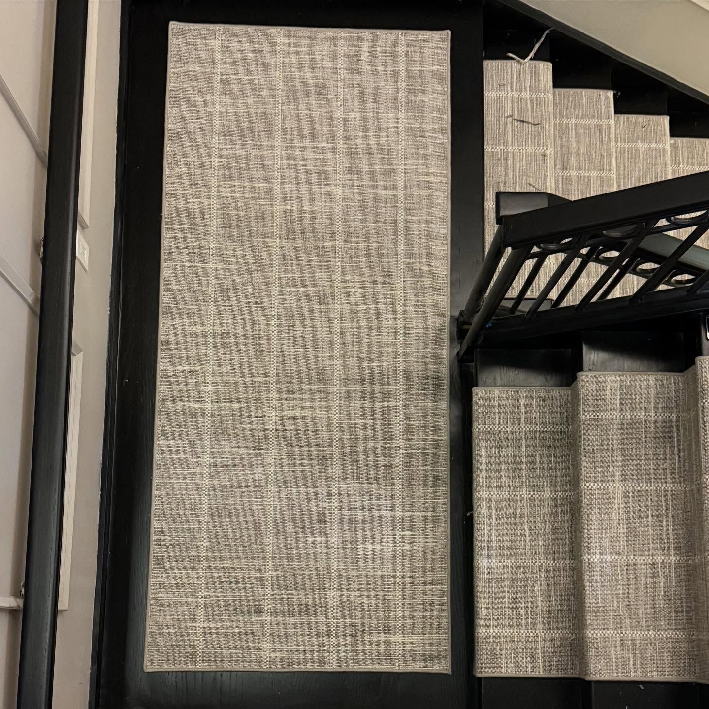 Top-down view of a rectangular rug and stair runners, all in a textured grey pattern, on black stairs.