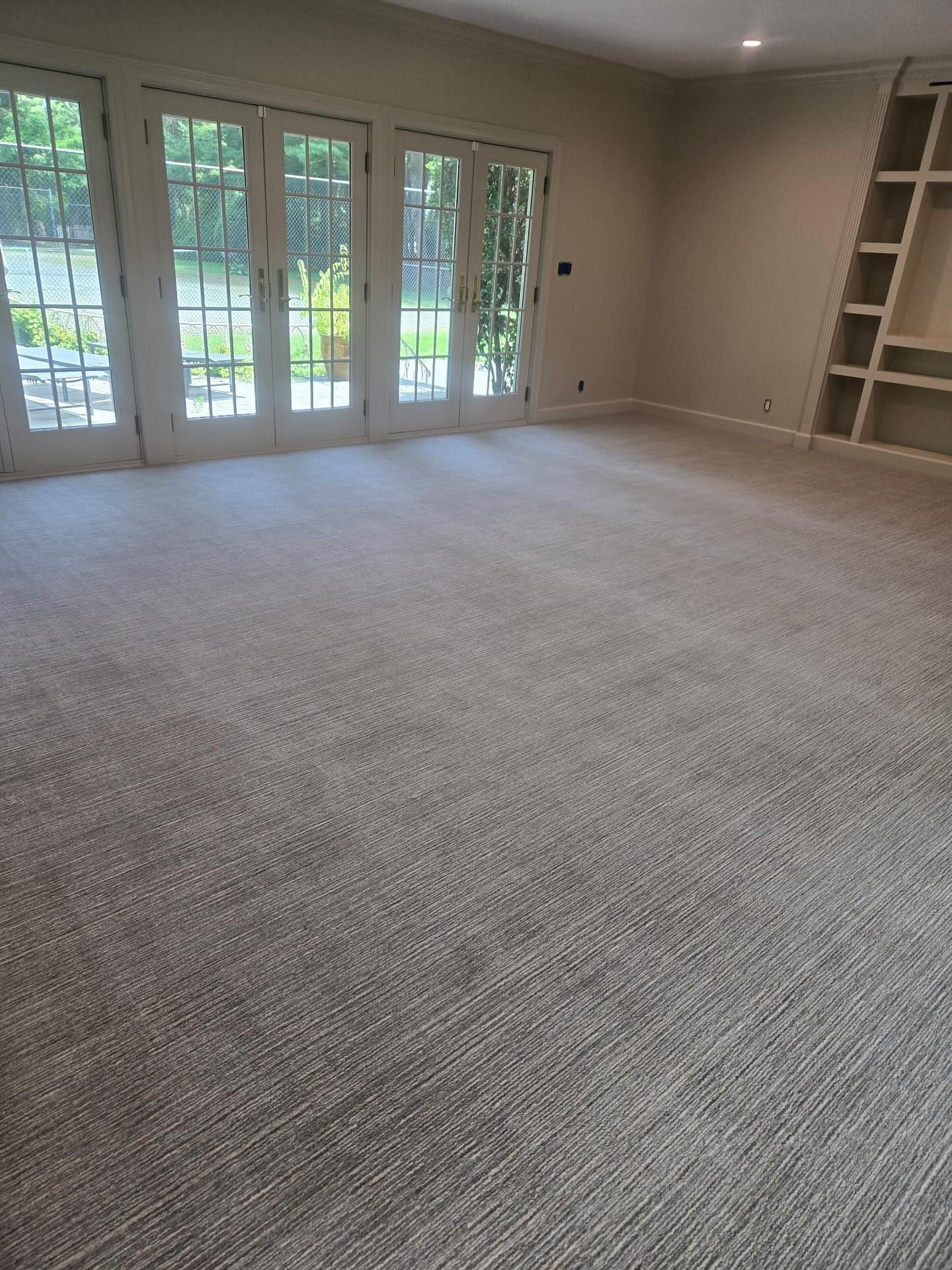 Spacious room with light beige carpet, French doors, and built-in shelving.