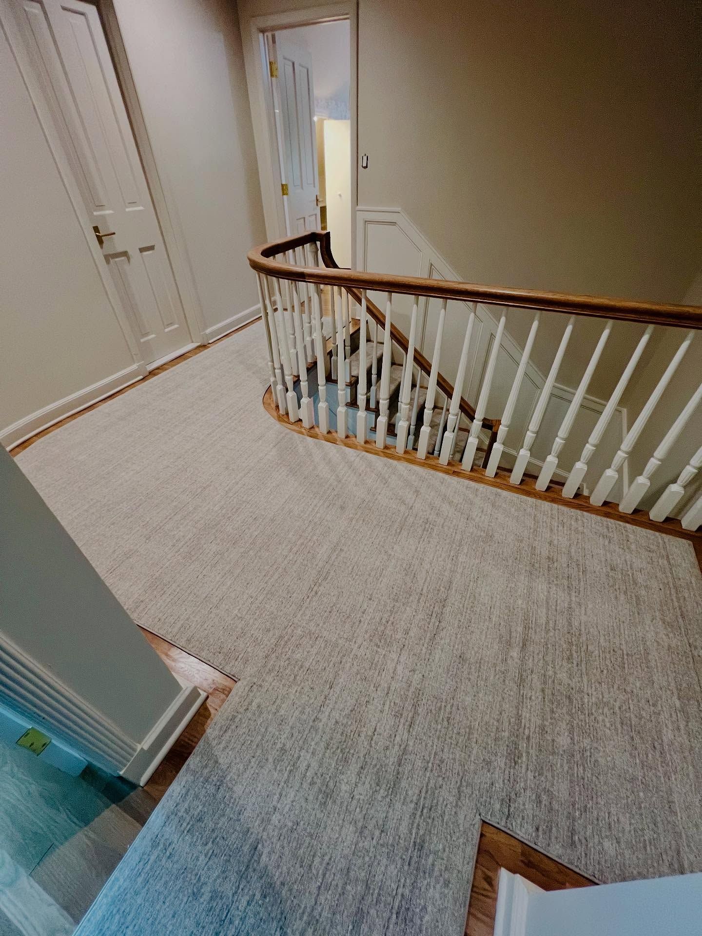 Hallway with carpeted floor, staircase with wood banister, and white doors.
