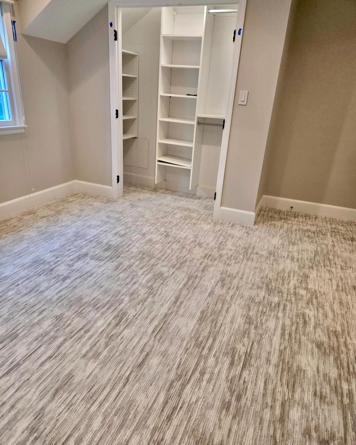 Bedroom with built-in white shelves and closet, beige walls, and patterned gray and white carpet.