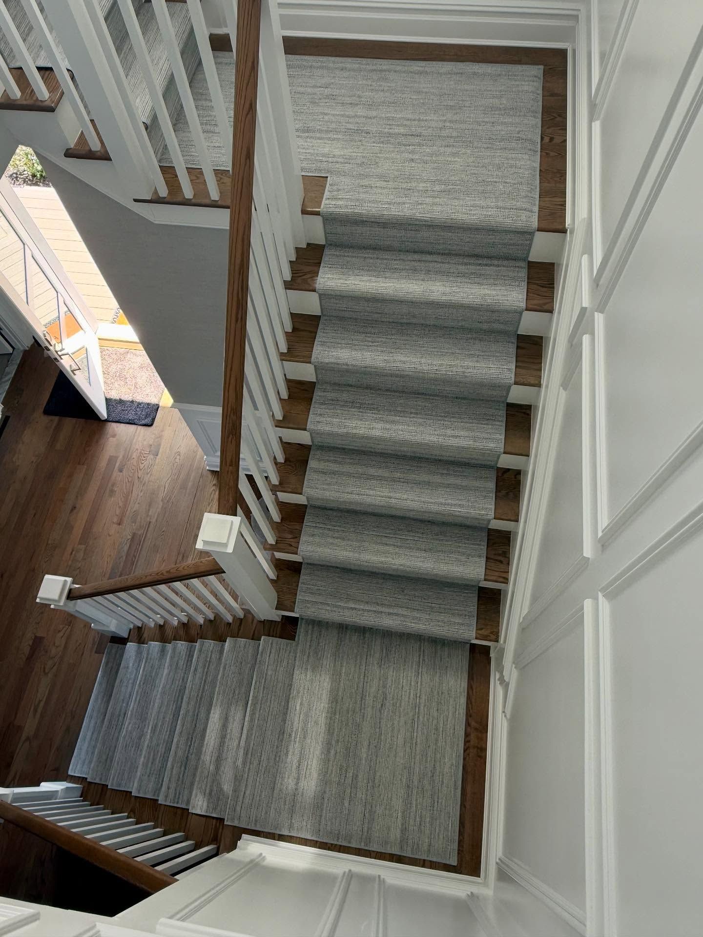 Staircase with gray runner rug and white banisters, brown wood stairs.