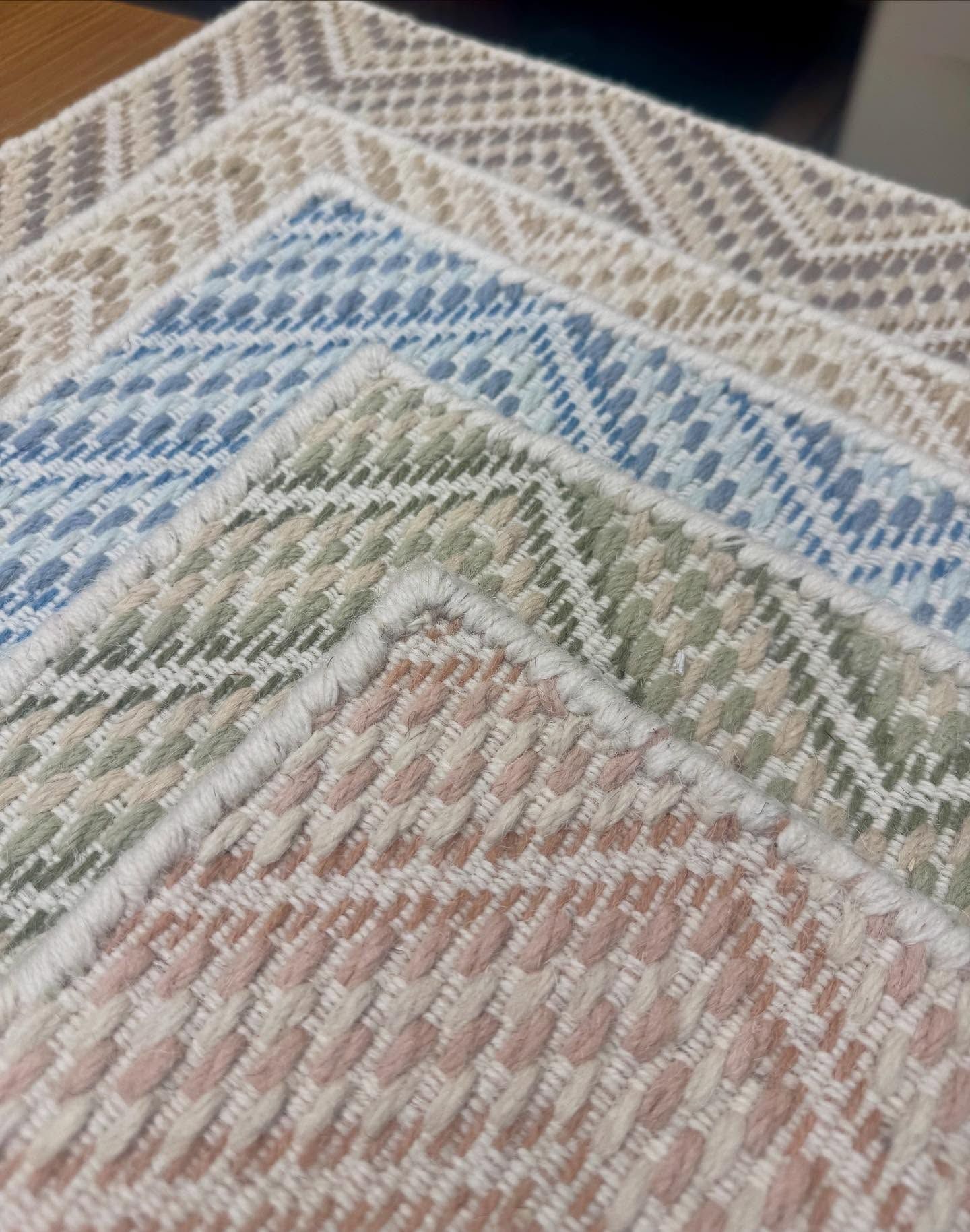 Close-up of a stack of woven placemats in pastel colors: pink, green, blue, tan, and gray.