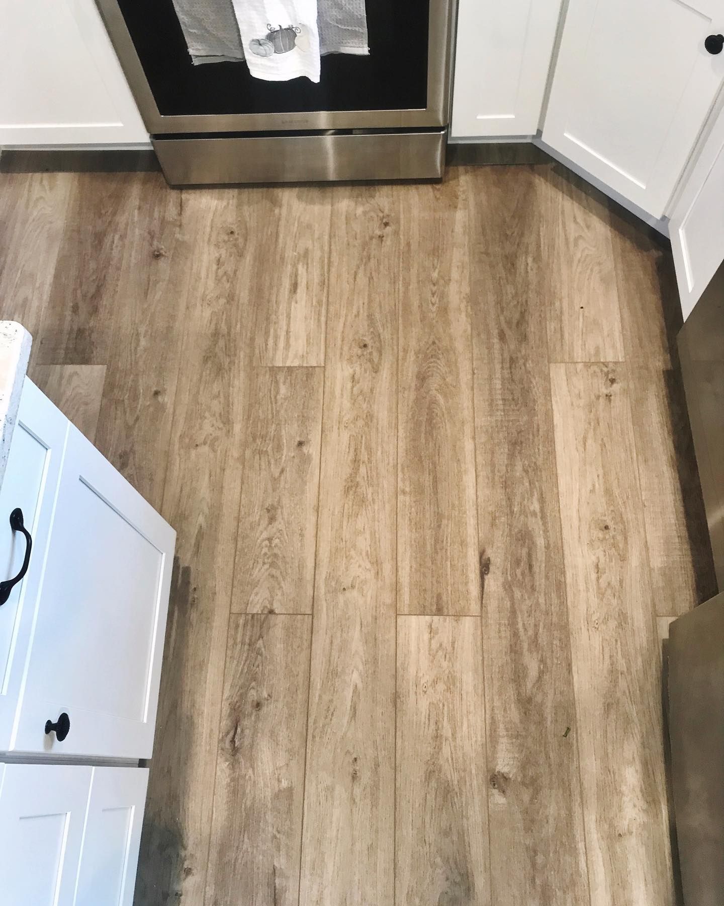 Light brown wood-look flooring in a kitchen, with white cabinets and a stainless steel oven.