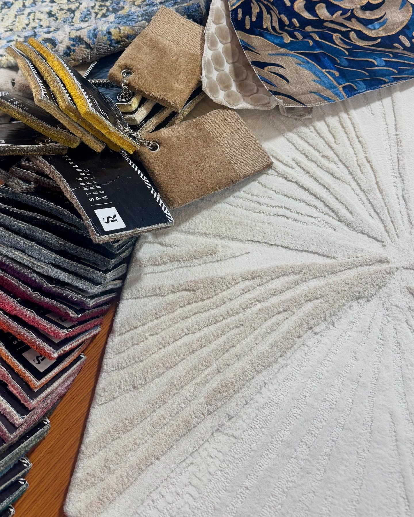 Assortment of fabric swatches and rugs in various colors and patterns, including blue, beige, and patterned textures.