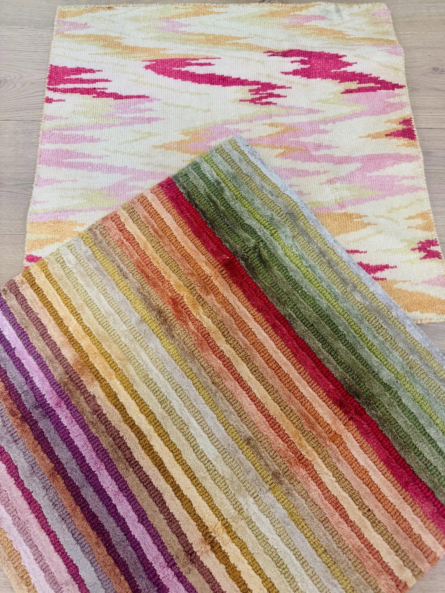 Two colorful woven rugs, one with pink zigzag pattern, the other with striped red, green, and yellow hues.