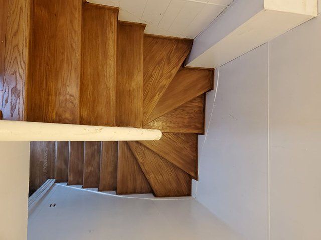 A wooden spiral staircase in a room with a white wall.