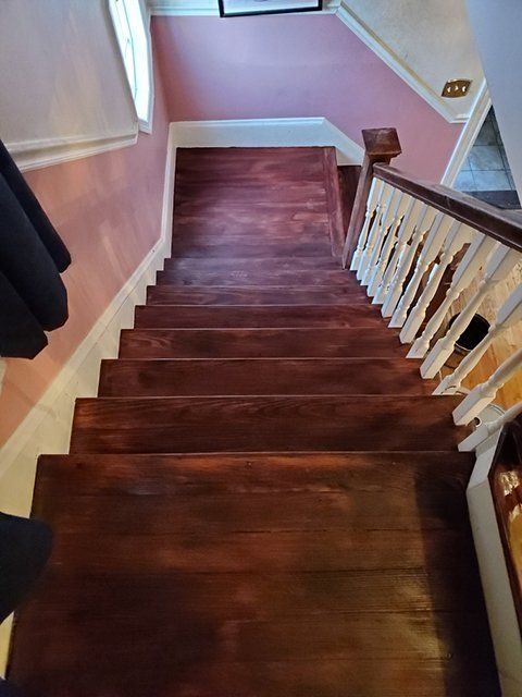 A wooden staircase with a white railing and a pink wall.