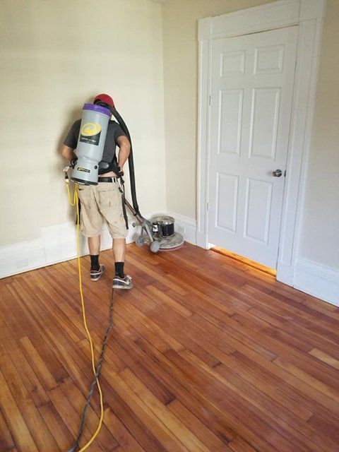 A man is using a vacuum cleaner on a wooden floor