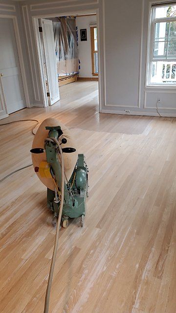 A machine is sanding a wooden floor in an empty room.