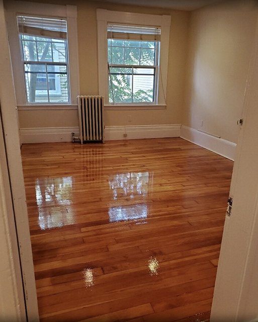 An empty living room with hardwood floors and two windows.