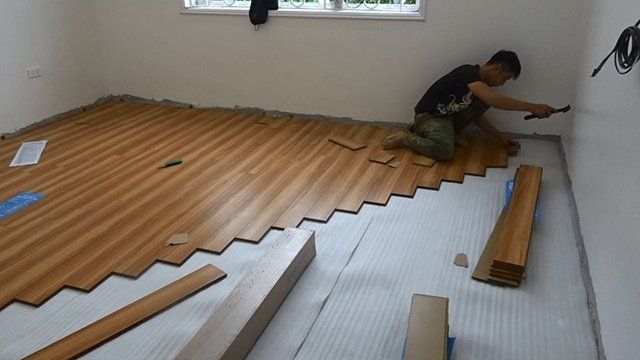 A man is installing a wooden floor in a room.