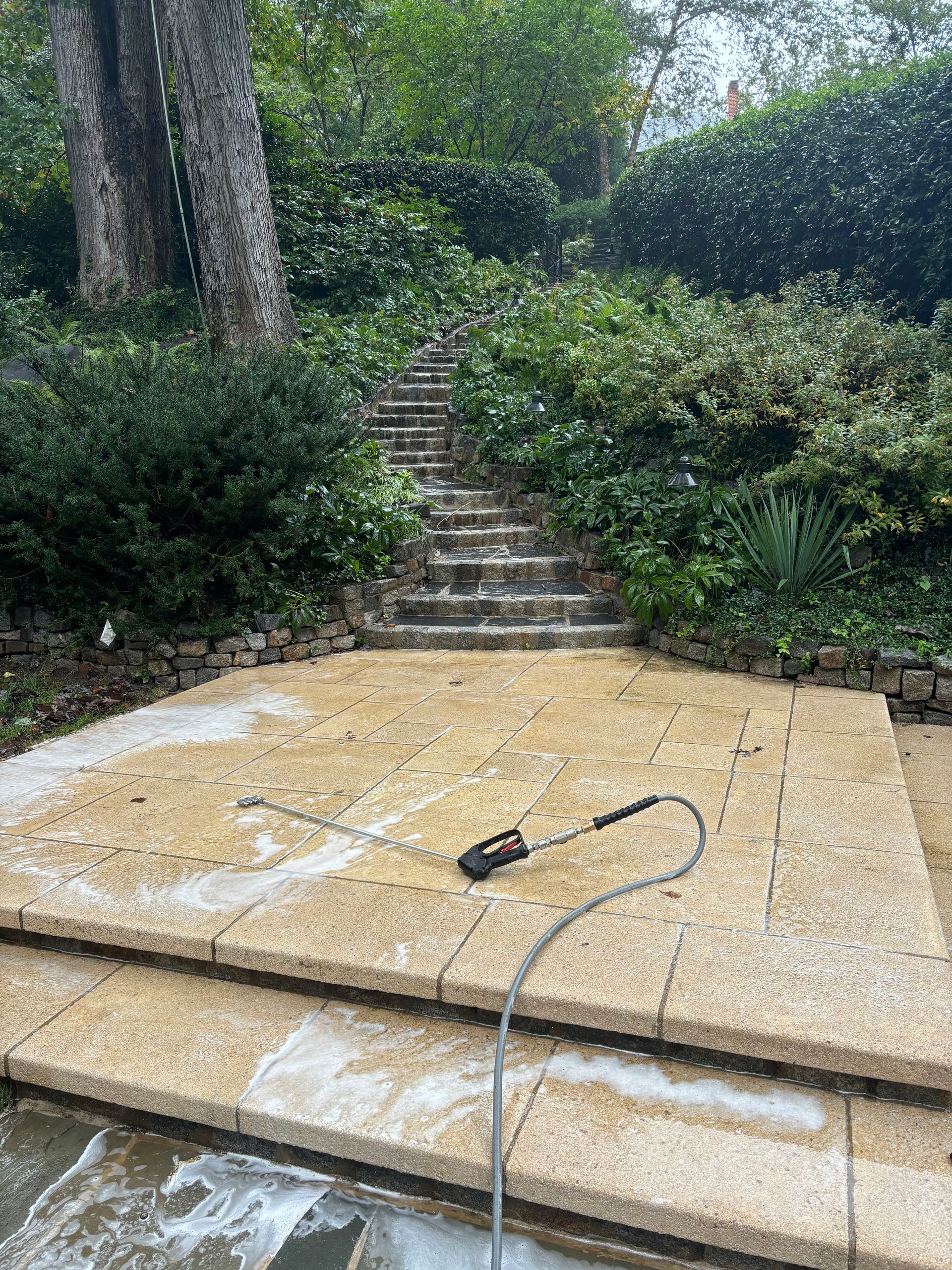 A pressure washer is cleaning a patio with stairs in the background.