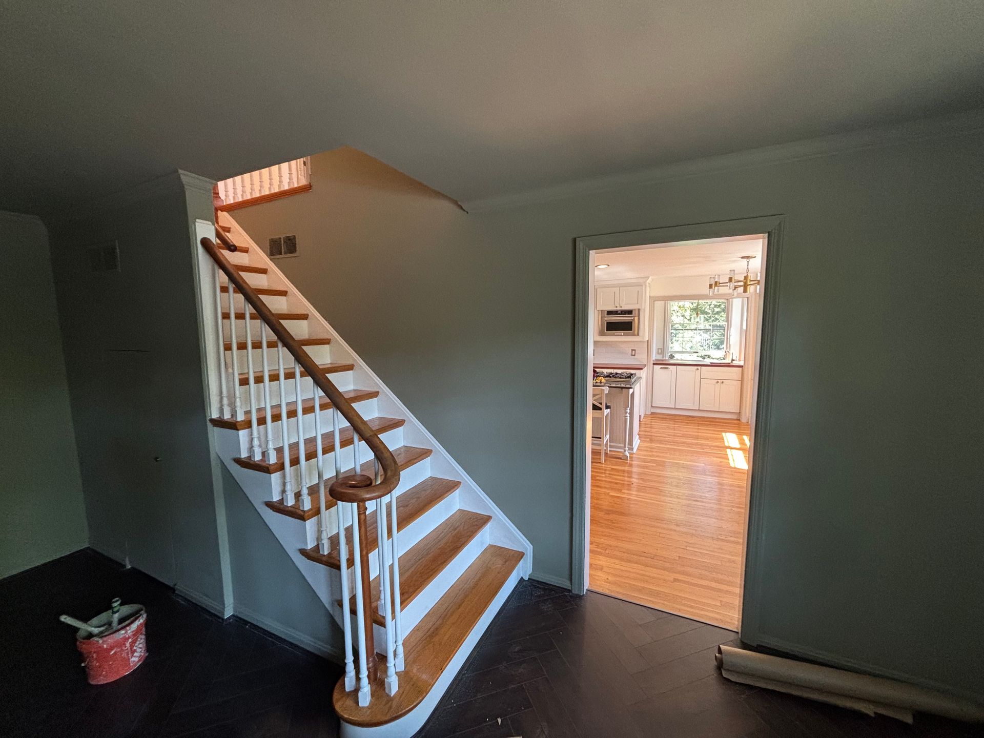 Staircase with wooden steps and white railing. Leads to an upper level. Doorway to a kitchen visible.
