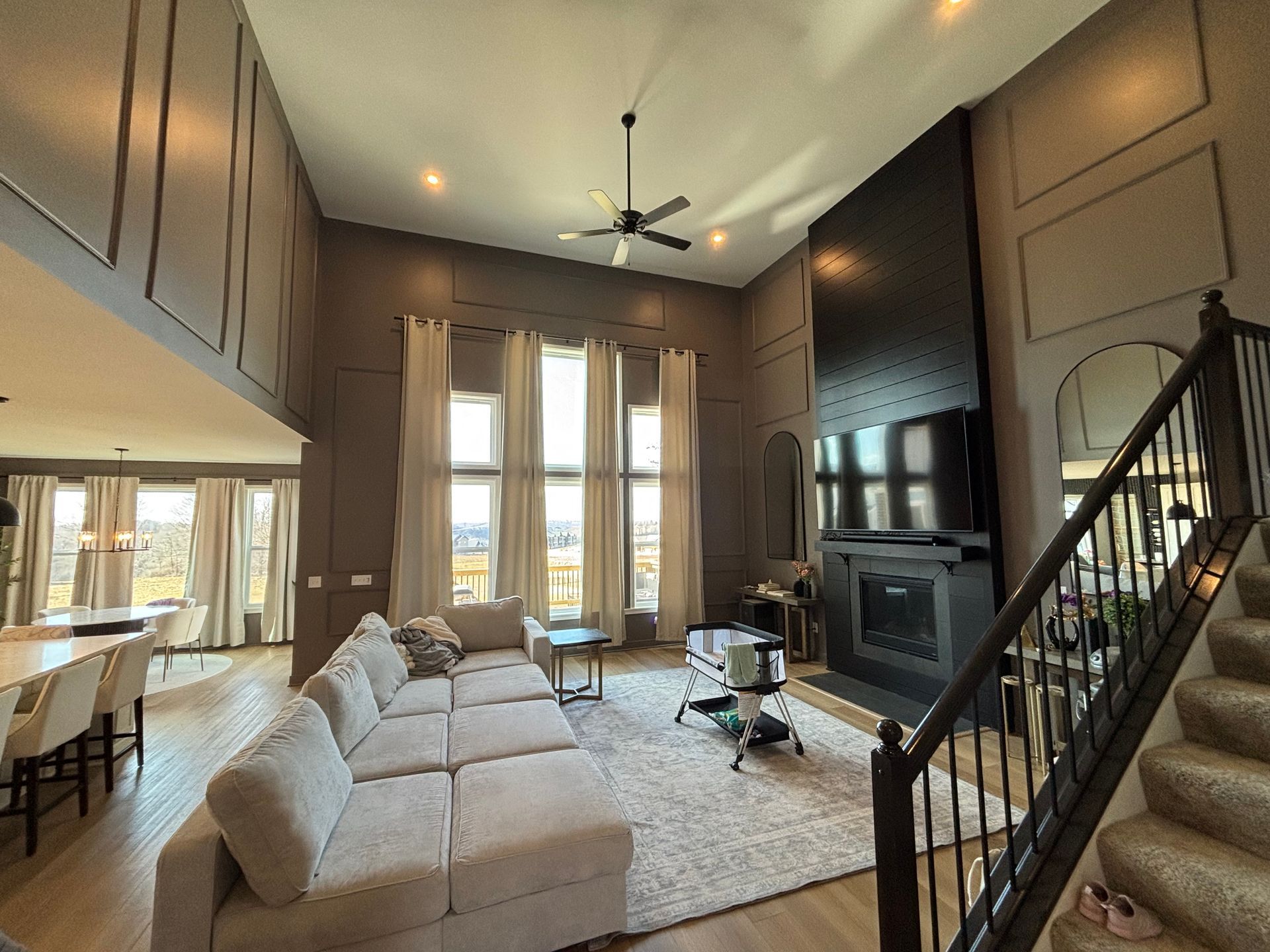 Spacious living room with high ceilings, large windows, fireplace, and staircase. Neutral colors and modern design.