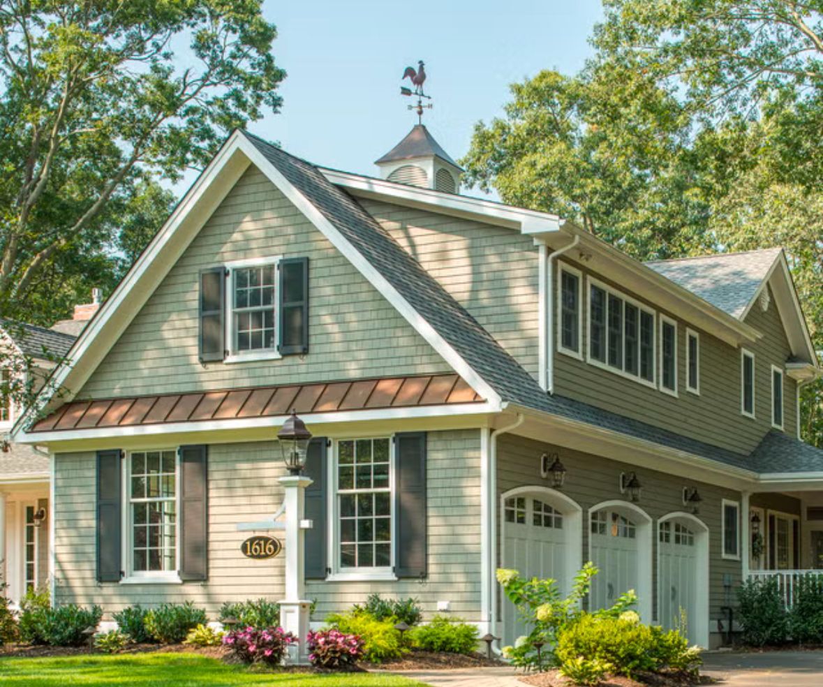 Green and white two-story house with three garage doors, a weathervane, and black shutters.