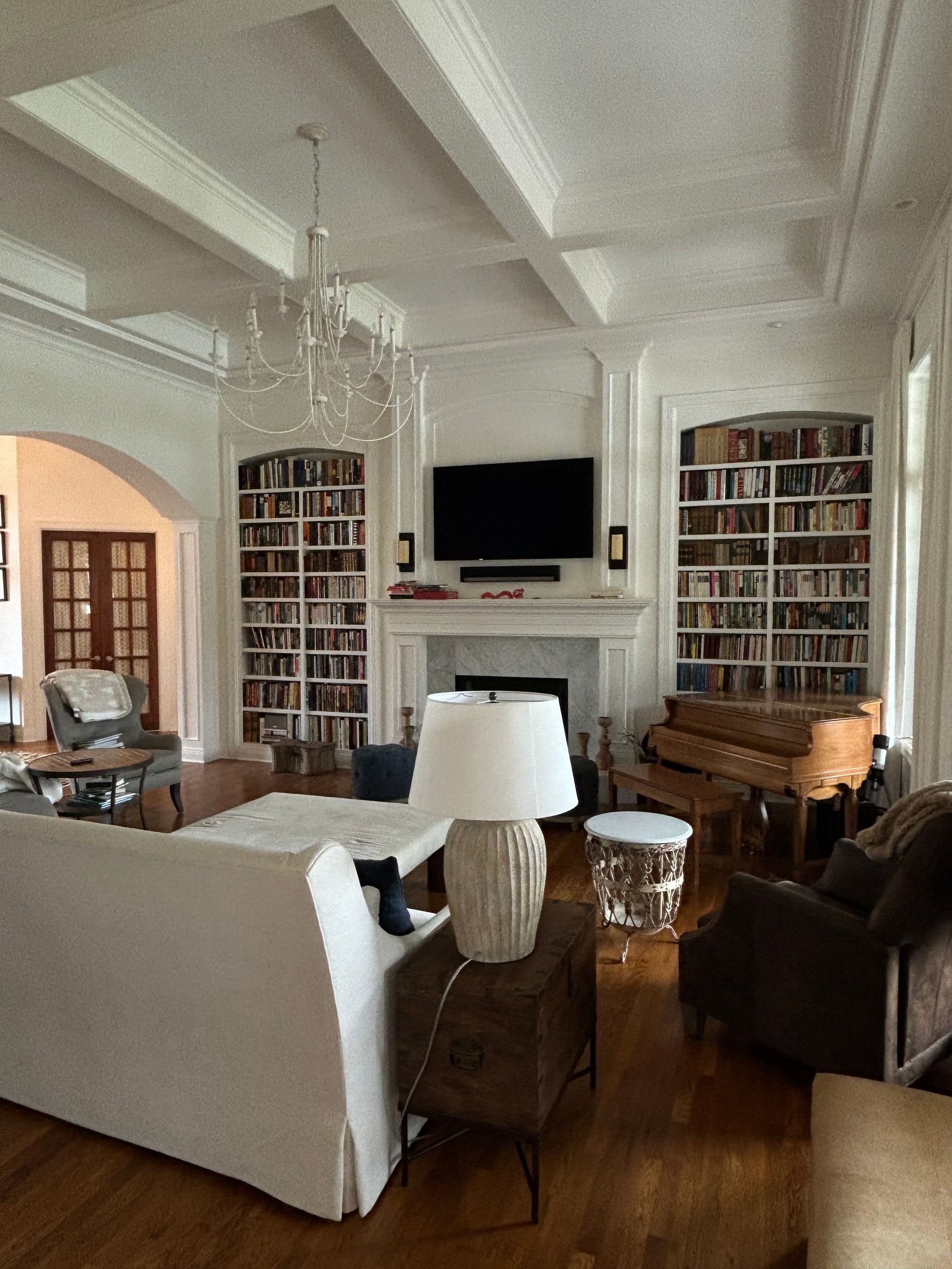 Living room with built-in bookshelves, fireplace, TV, chandelier, and white sofa.