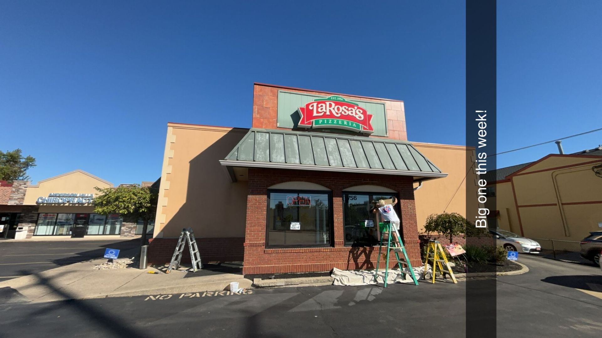 Pizza restaurant with a green sign under a blue sky, construction underway.