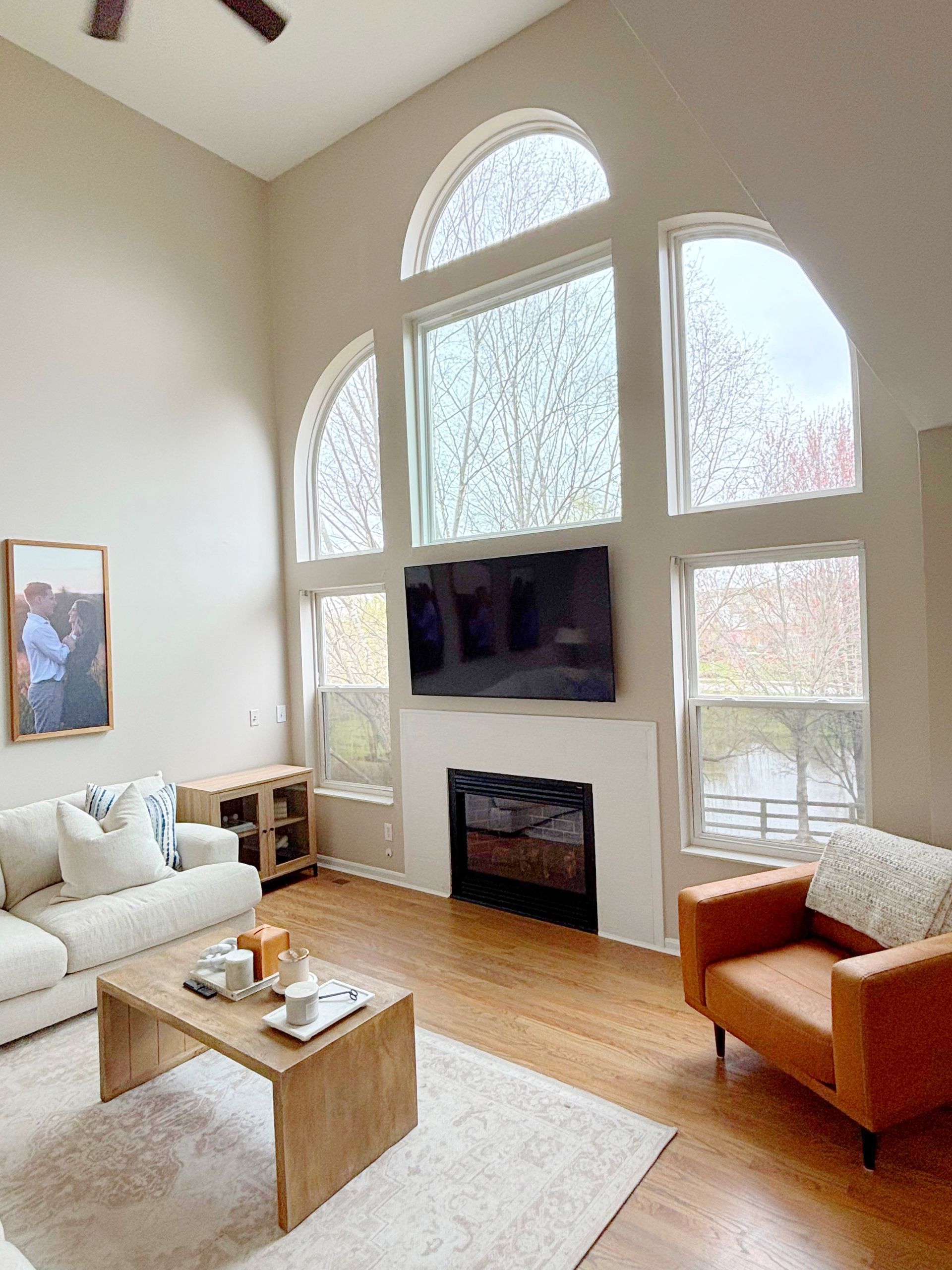 Living room with high ceilings, large arched windows, fireplace, TV, sofa, and armchair.