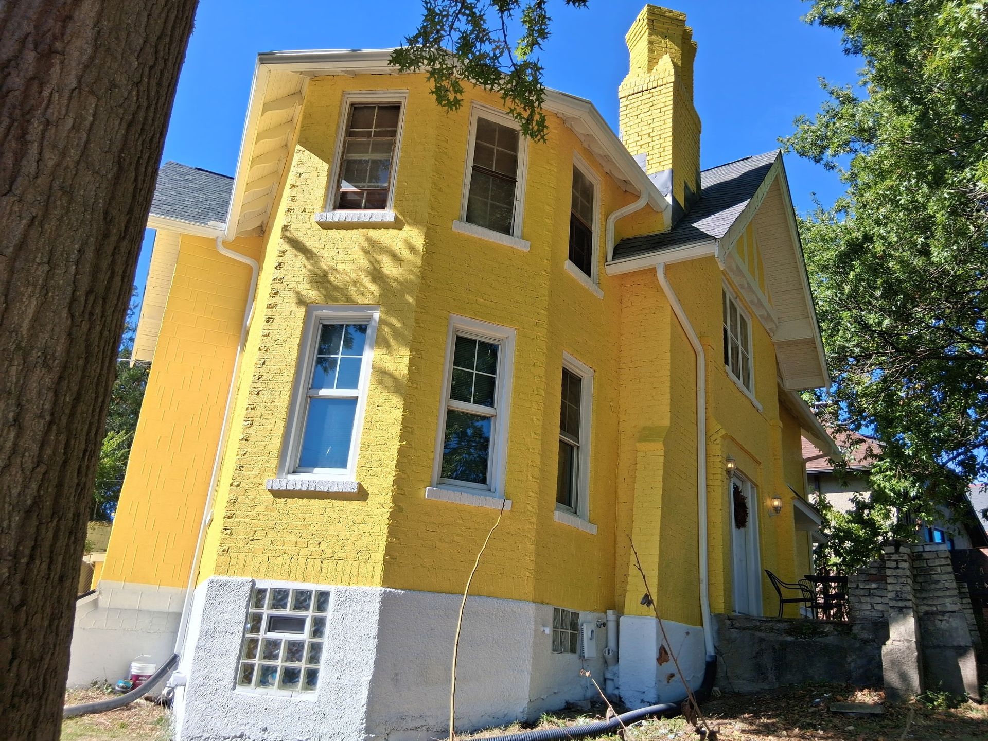 Yellow two-story house with white trim and a prominent chimney against a blue sky.