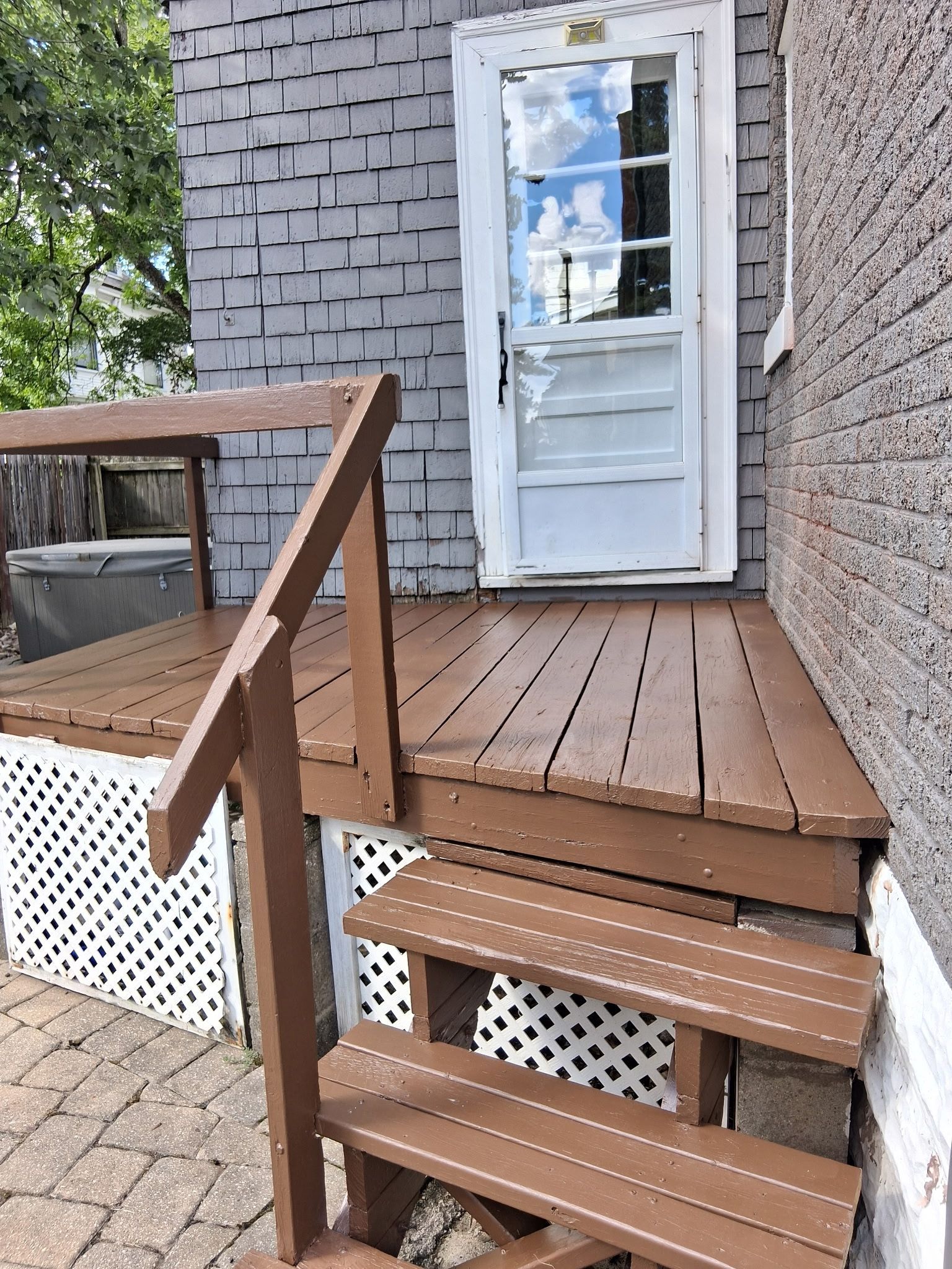 Brown wooden deck and stairs leading to a white door with glass panels. Grey shingled siding.