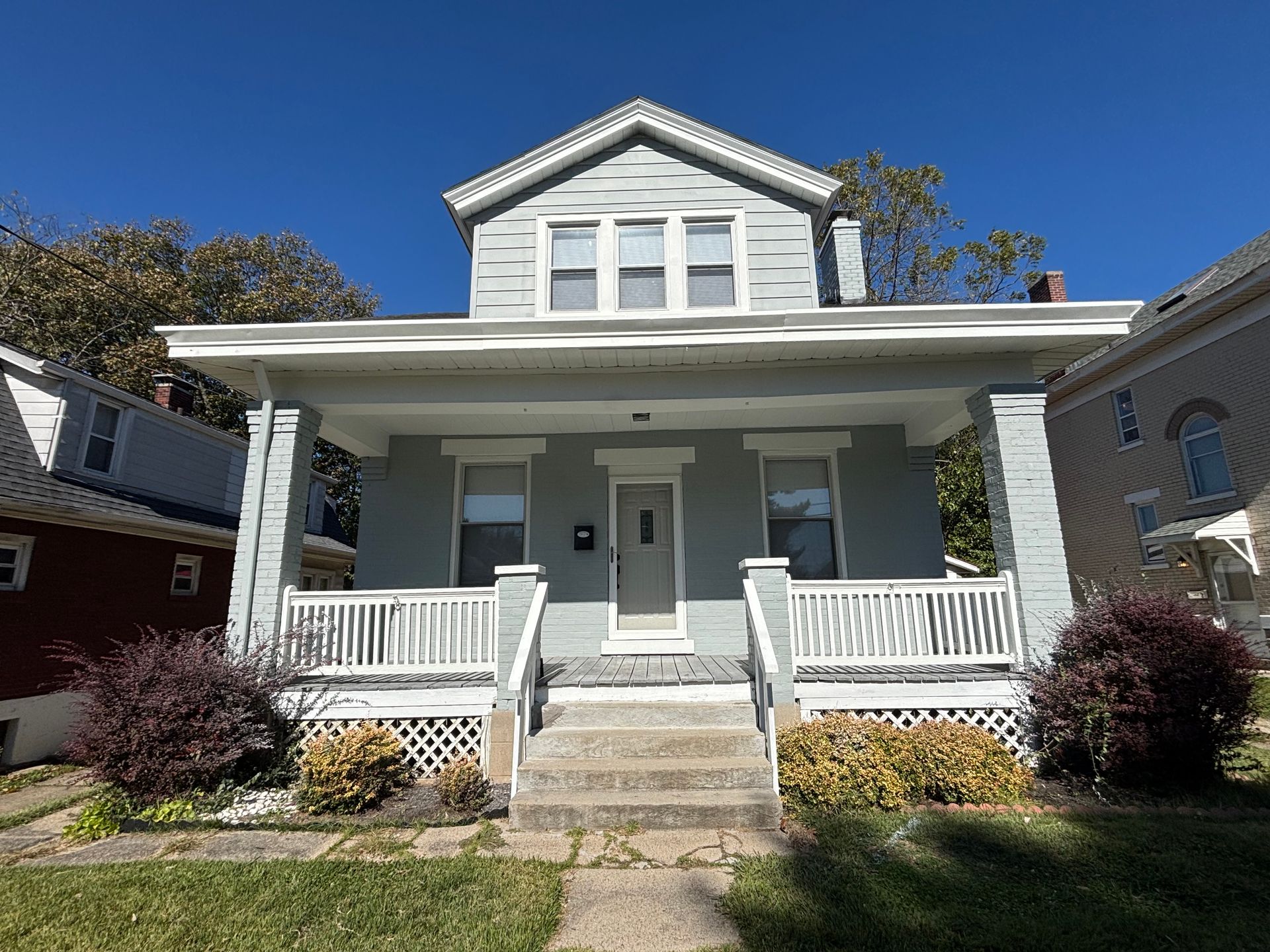 Two-story house with light blue siding, white porch, and gray steps under a blue sky.