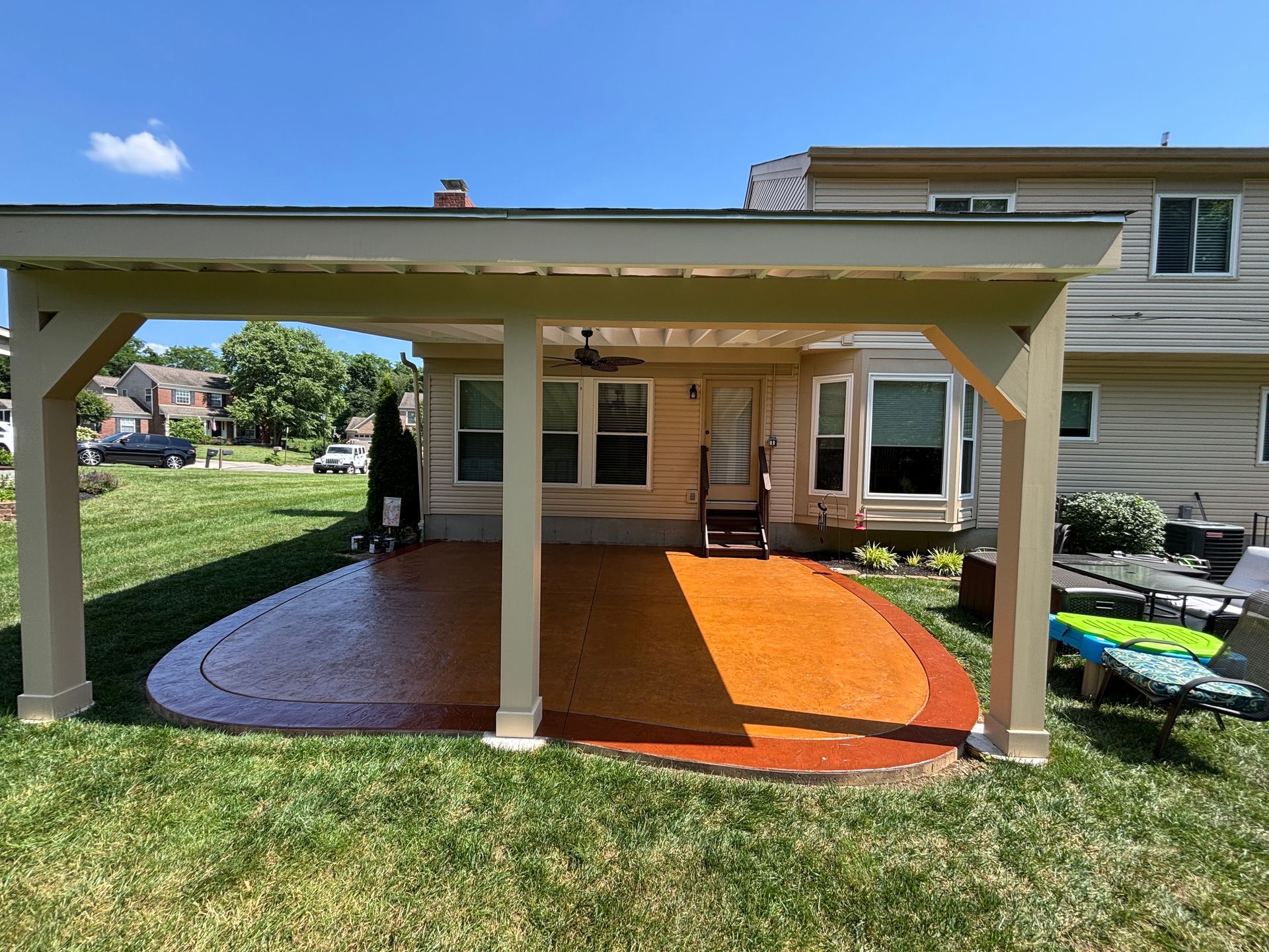Pergola over a stamped concrete patio, adjacent to a beige house, in a grassy backyard.