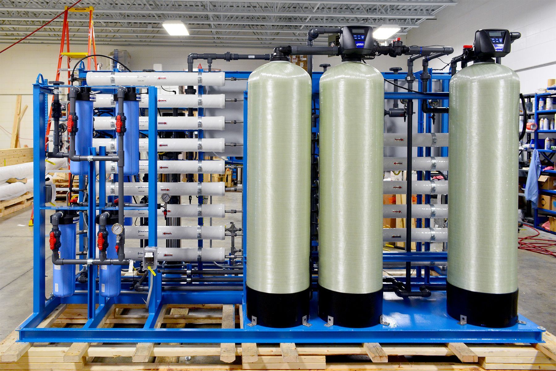 Industrial water filtration system with blue piping and three large white tanks on a factory pallet.
