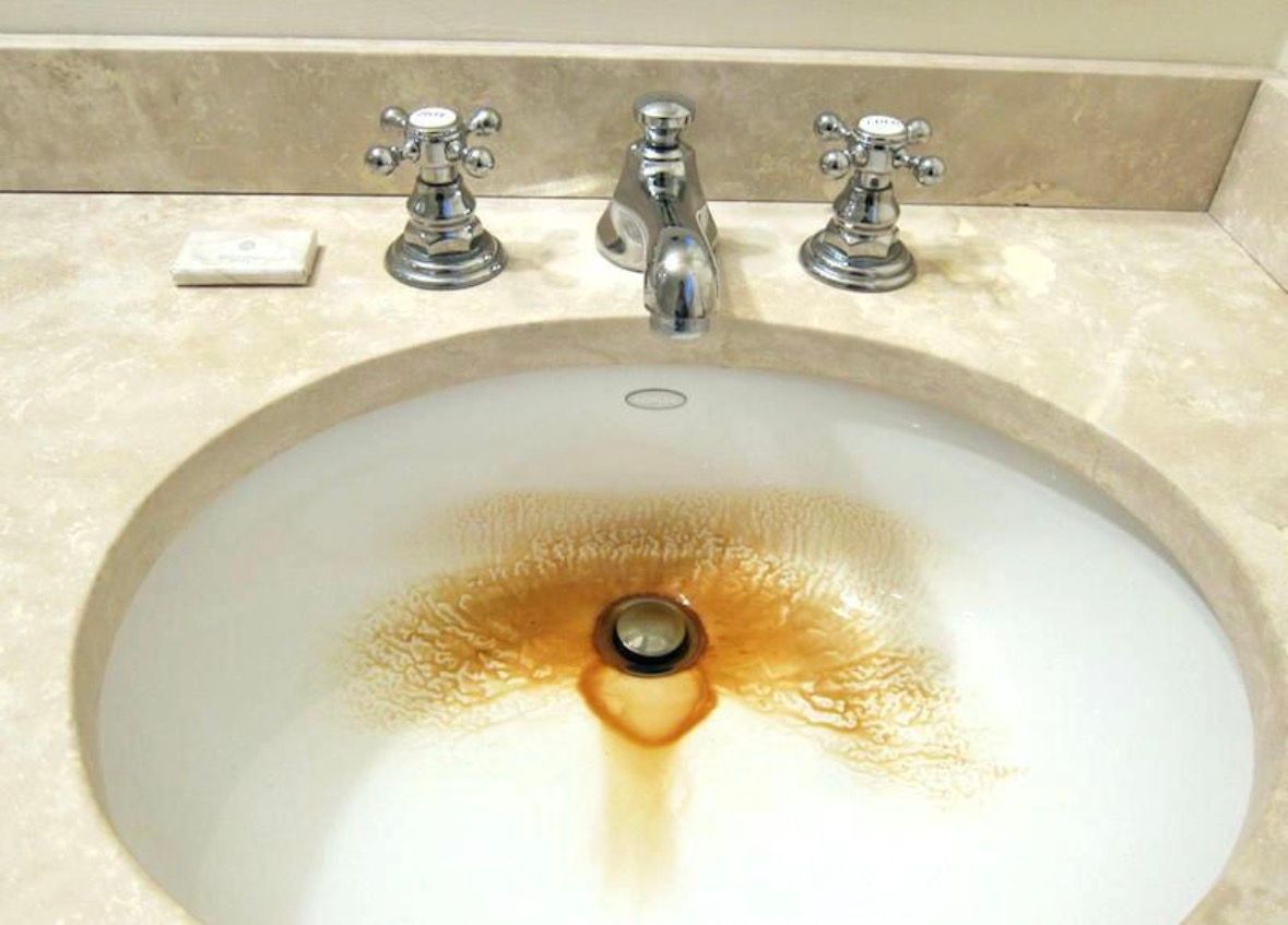 Bathroom sink with rust-stained water around the drain and chrome faucets above.