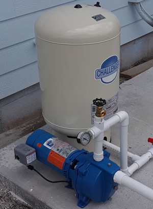 Blue well pump and beige pressure tank beside a house exterior.