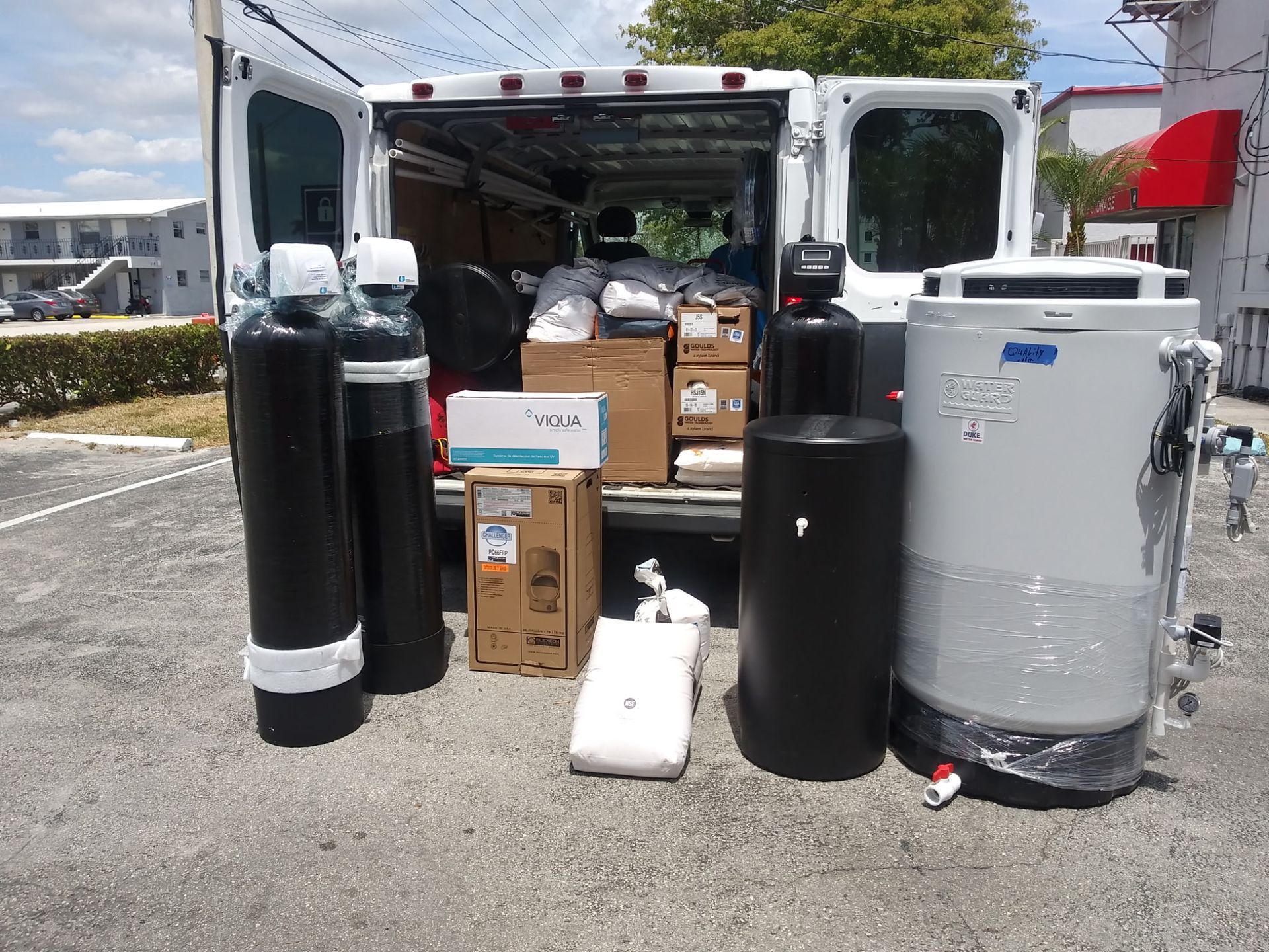 Open box truck with large black and silver cylinders and boxes loaded at the rear in a parking lot