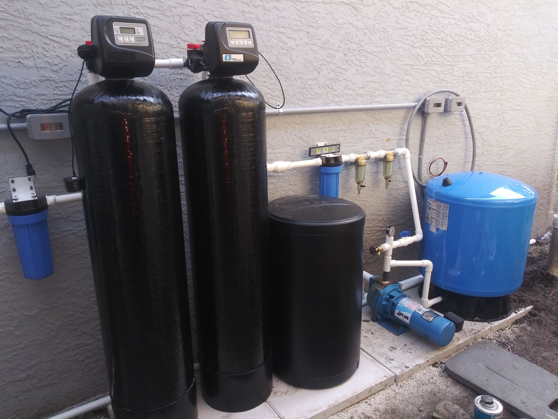 Water softener and filtration tanks with blue pressure tank in an outdoor utility area